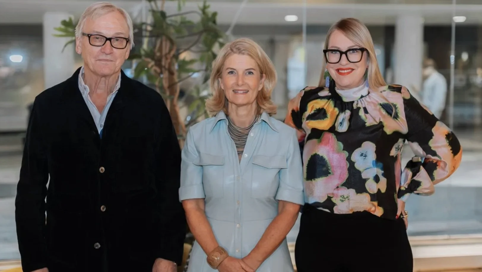 Tre personer står tillsammans i en modern inomhusmiljö, alla ler och tittar mot kameran.