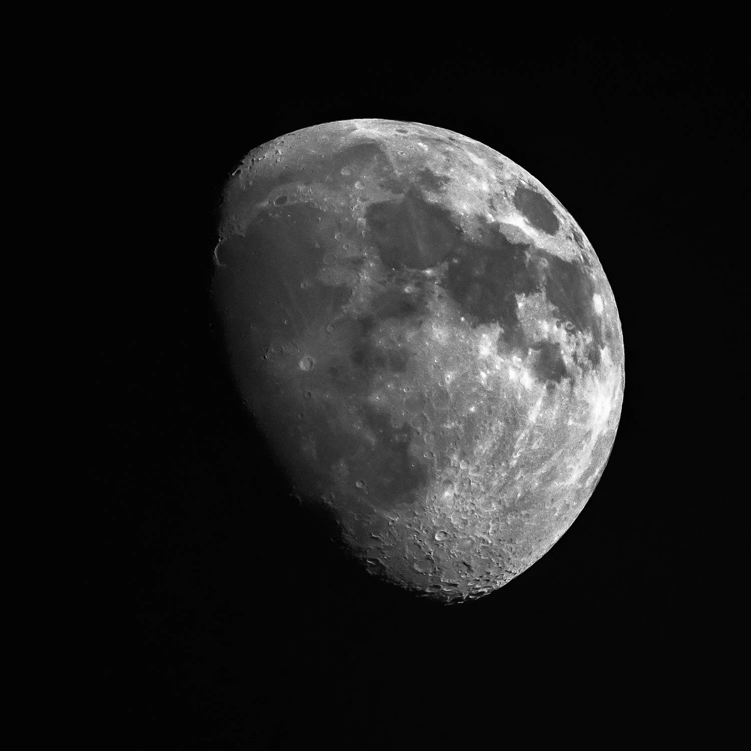 A detailed black-and-white photograph of the moon showing shadows, craters and rocky surface features against the dark night sky.