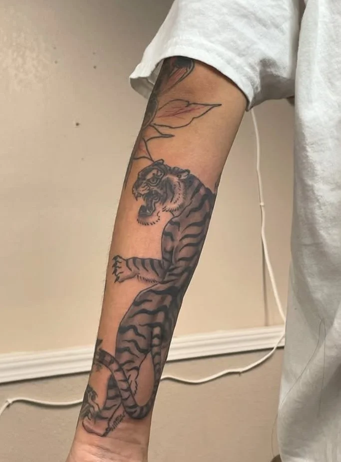 Forearm tattoo of a tiger with surrounding floral design.