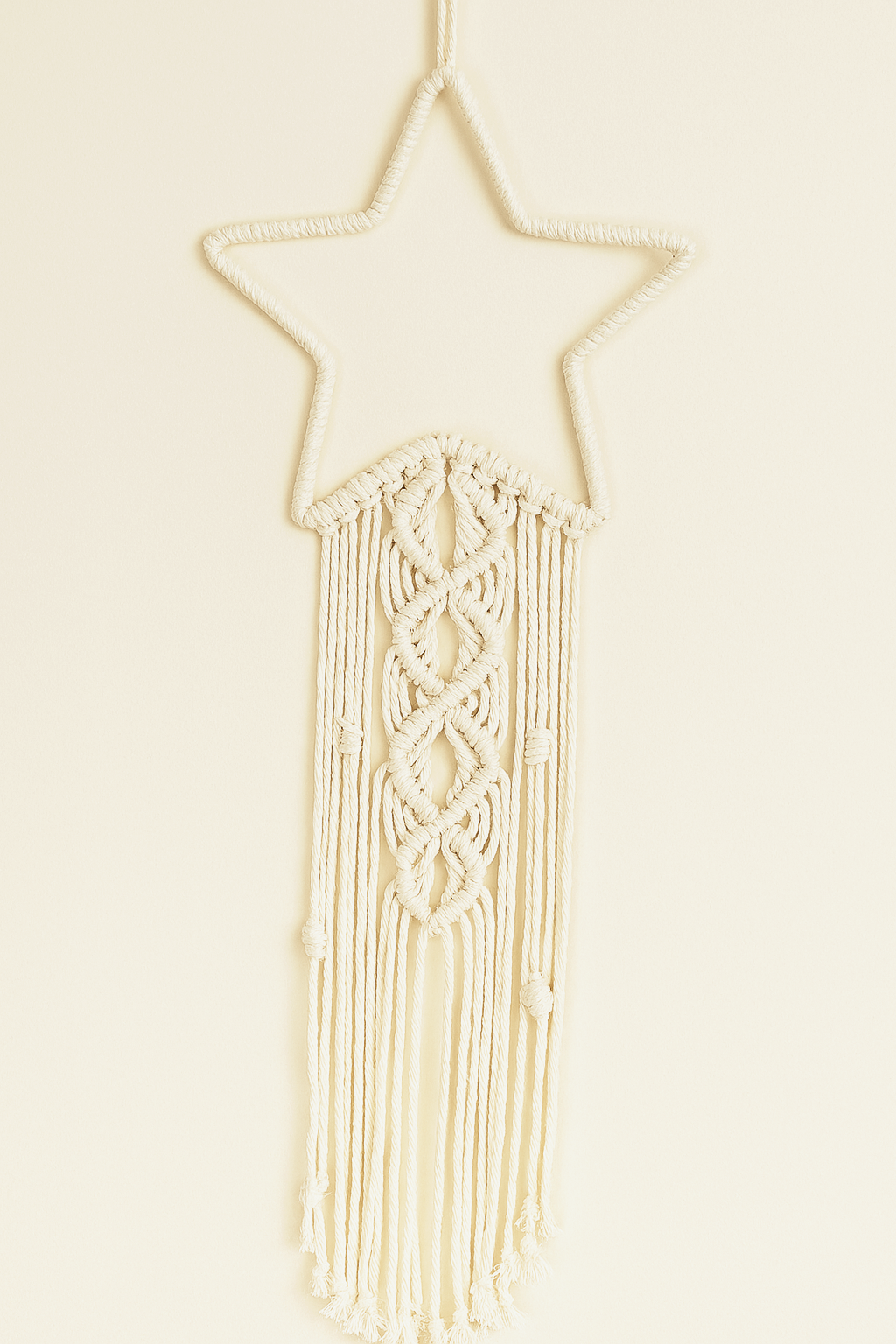 Handmade macramé star wall hanging in off-white cotton cord with elegant knotting and boho fringe design.