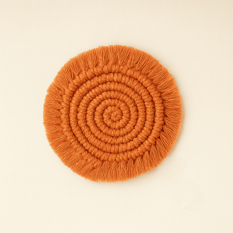 A handcrafted round macramé coaster in a warm terracotta color with a spiral design and fringe edges, lying flat on a beige textile background with a "Samra Knots" label.