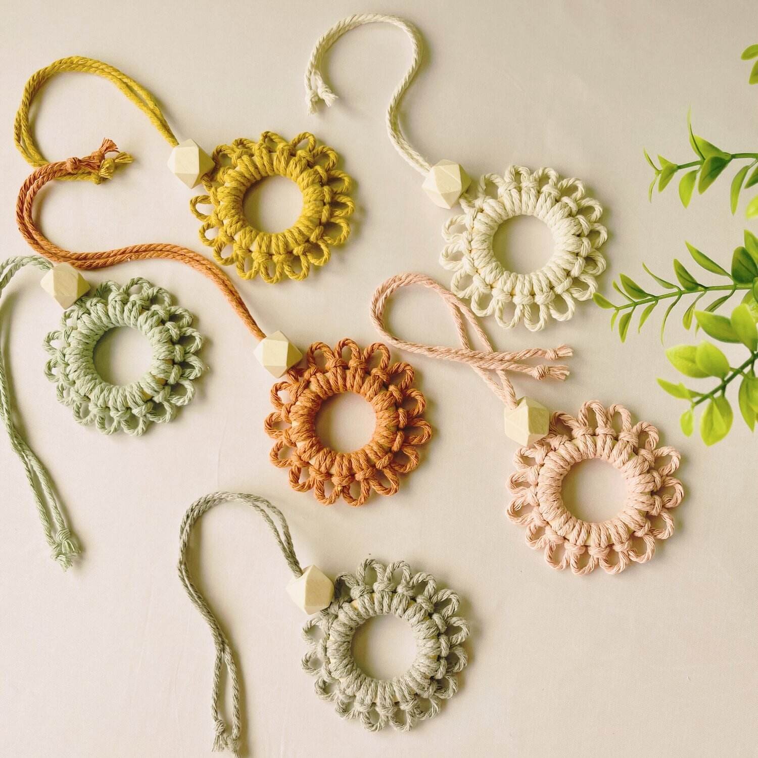 Handmade macramé car diffuser keychains in soft pastel and earthy tones, featuring wood scent beads – styled flatlay on off-white background by Samra Knots.