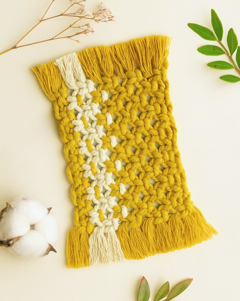 Handmade mustard macramé mugrug with off-white accent stripe, styled with dried flowers and Samra Knots tag on a soft beige background.
