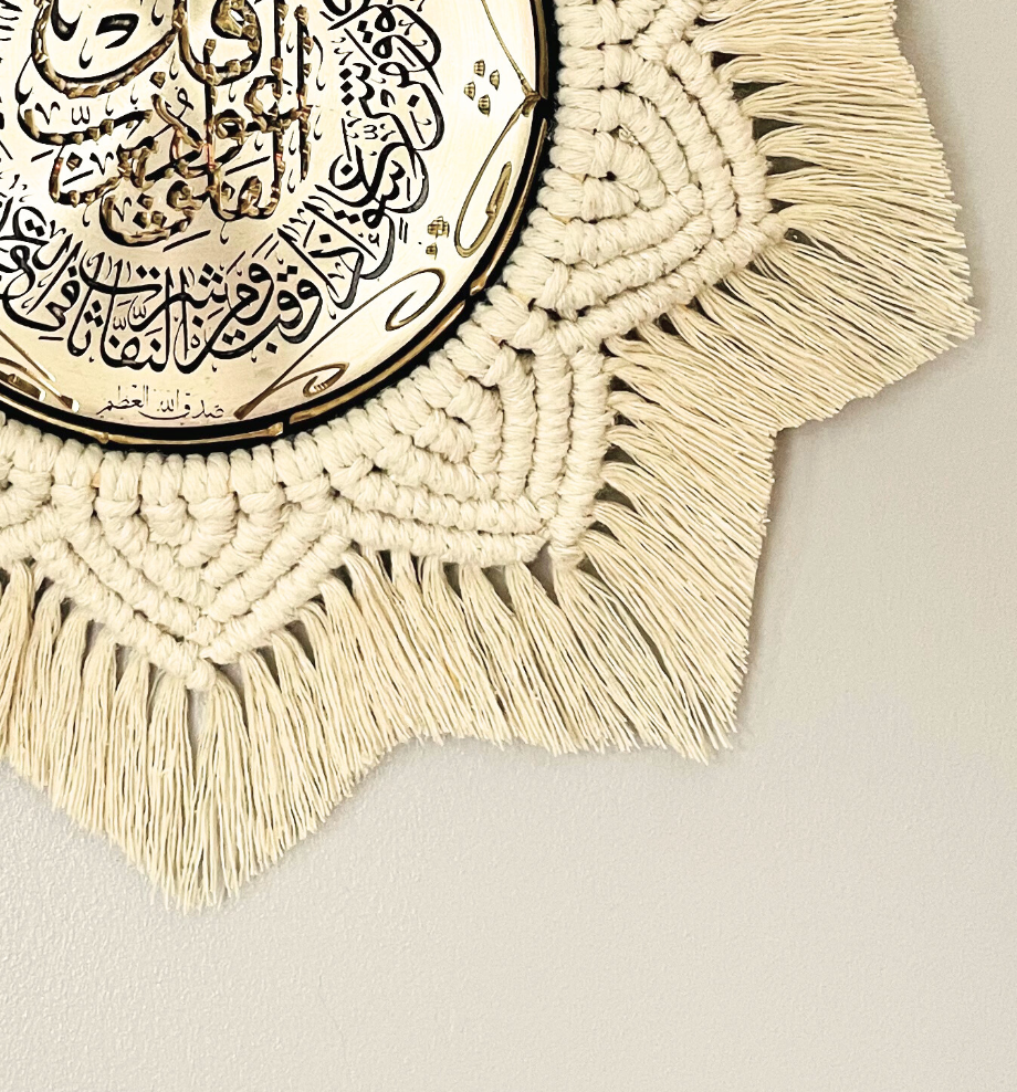 Detailed view of off-white macramé knots and fringe surrounding the gold Arabic calligraphy plate in a handmade wall decor piece