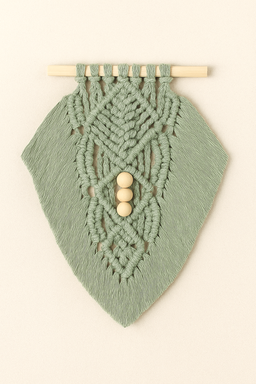Boho macramé wall hanging in muted sage green, featuring leaf-inspired knots and three wooden beads, photographed on neutral backdrop.