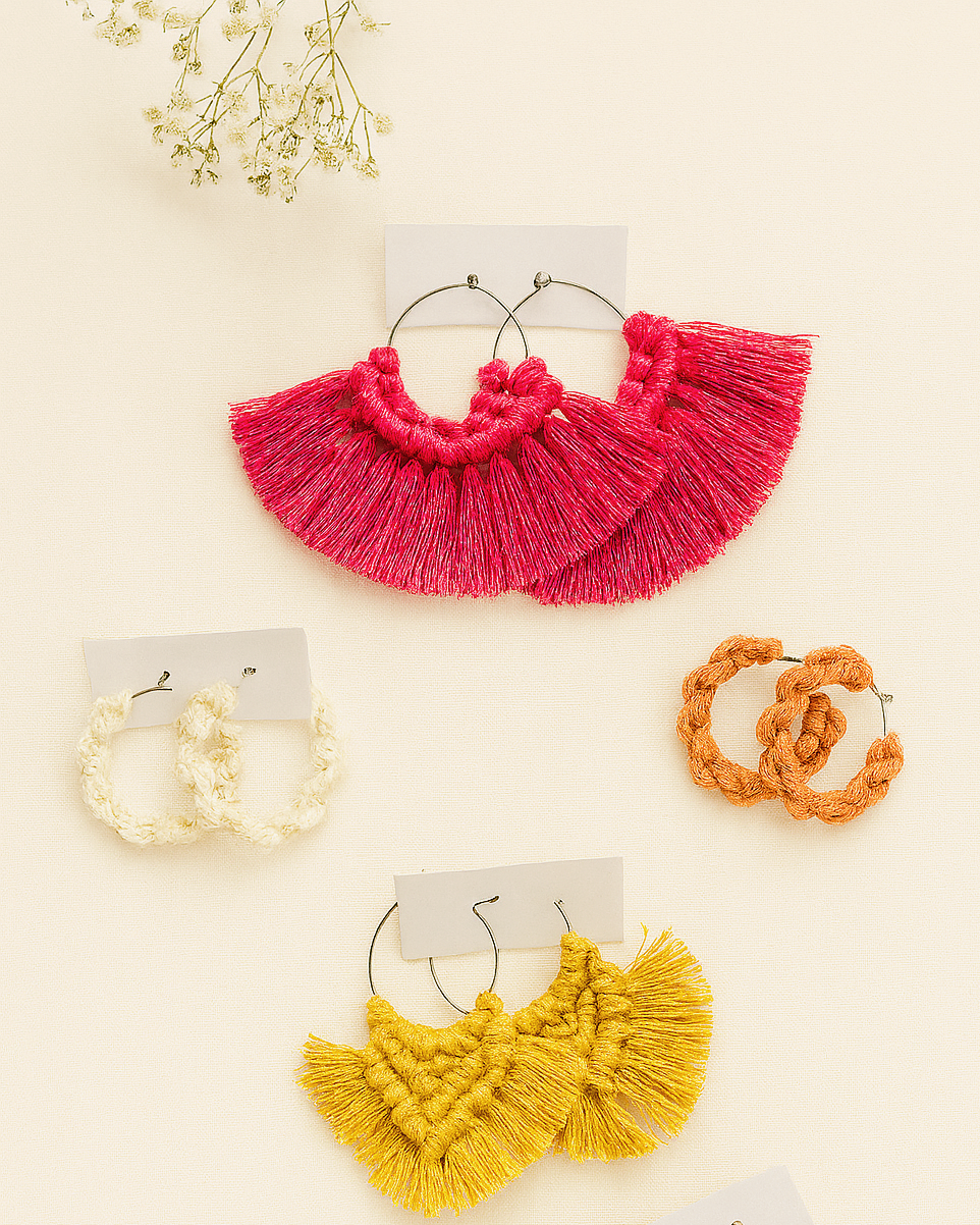 Four pairs of handmade macramé hoop earrings in pink, mustard yellow, terracotta, and off-white displayed on a neutral background with baby’s breath flowers