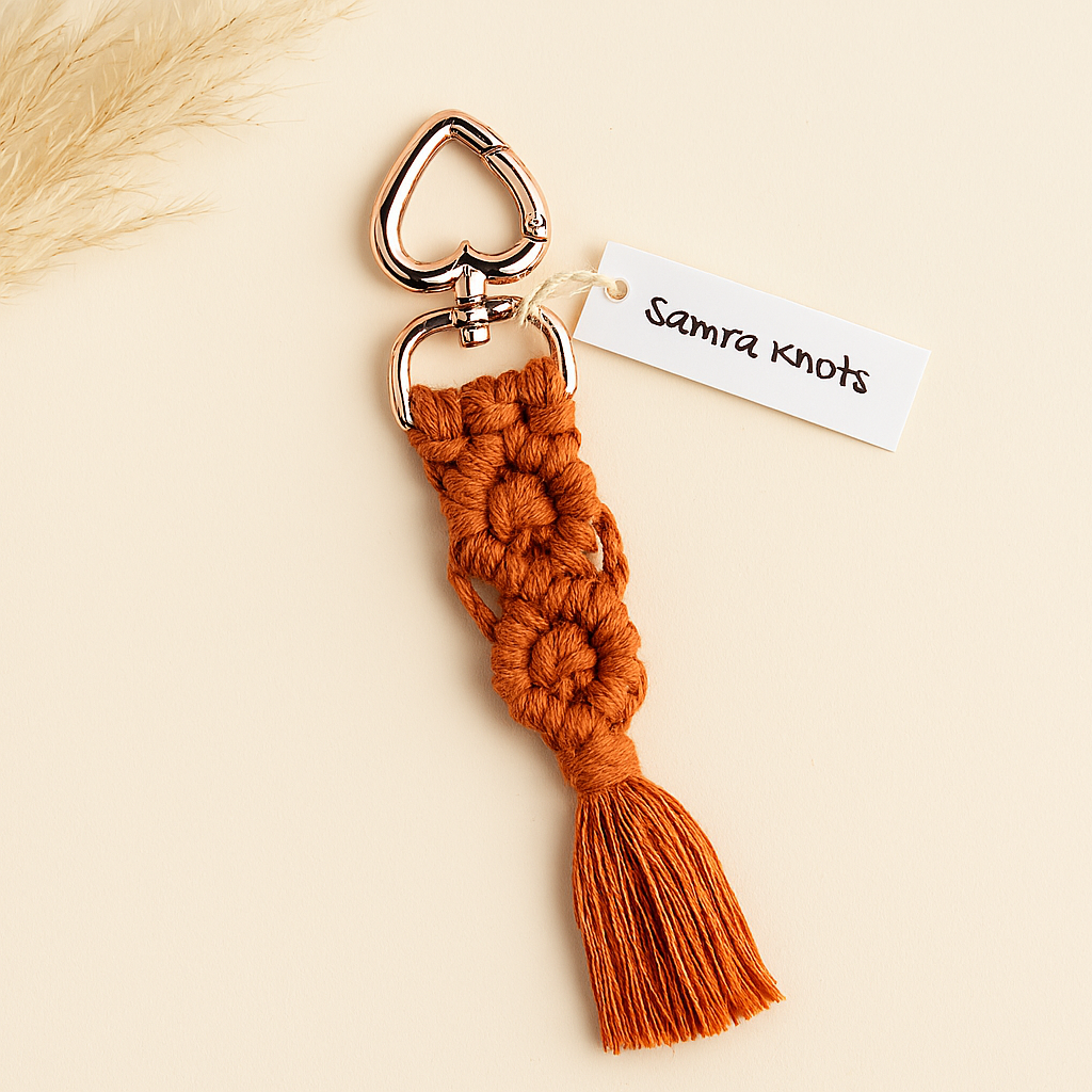 Terracotta handmade macramé keychain with rose gold heart clasp, styled with neutral pampas grass on an off-white background