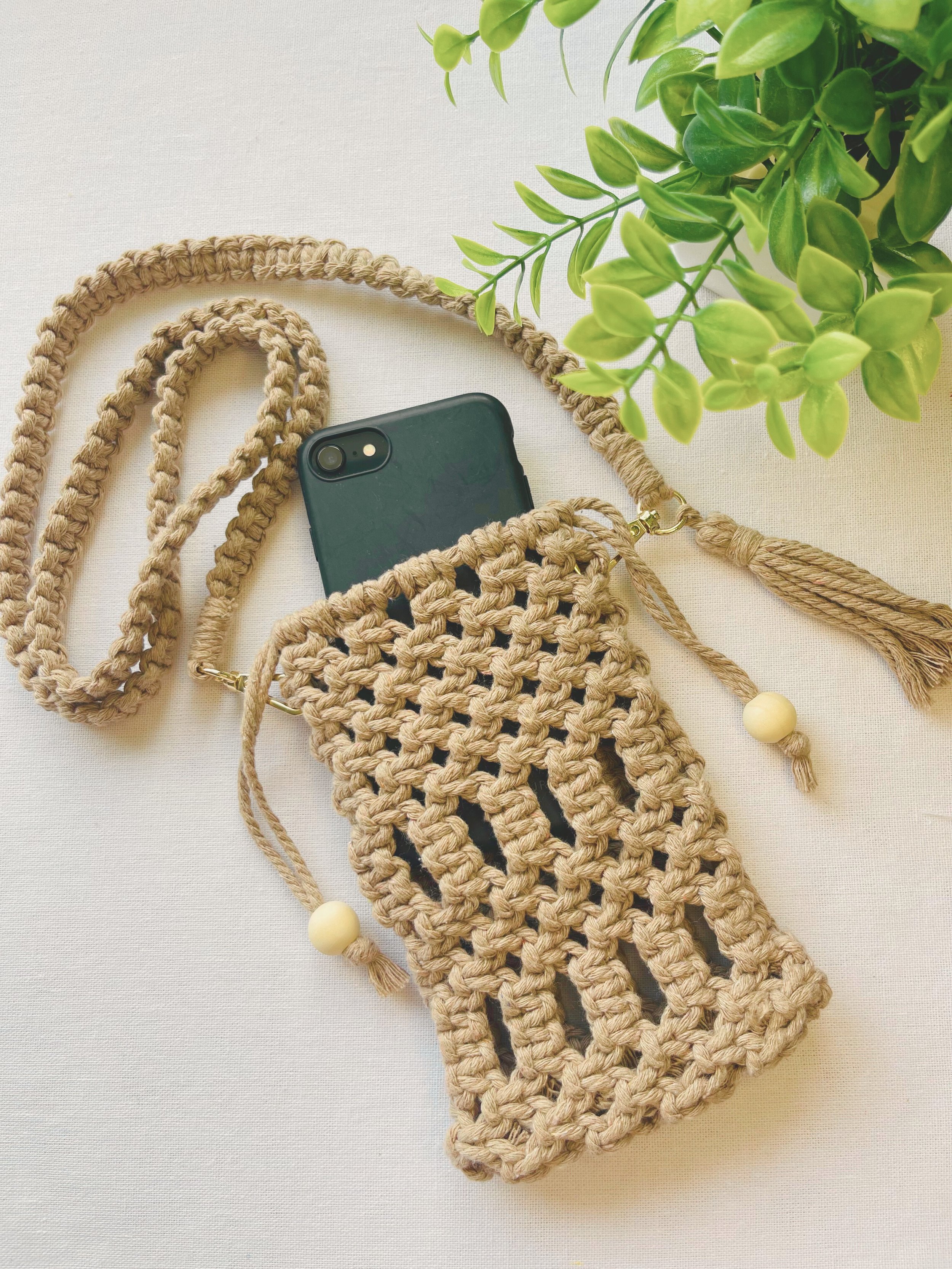 Handmade macramé phone bag in light brown cotton cord with phone inside, styled with braided strap and tassels