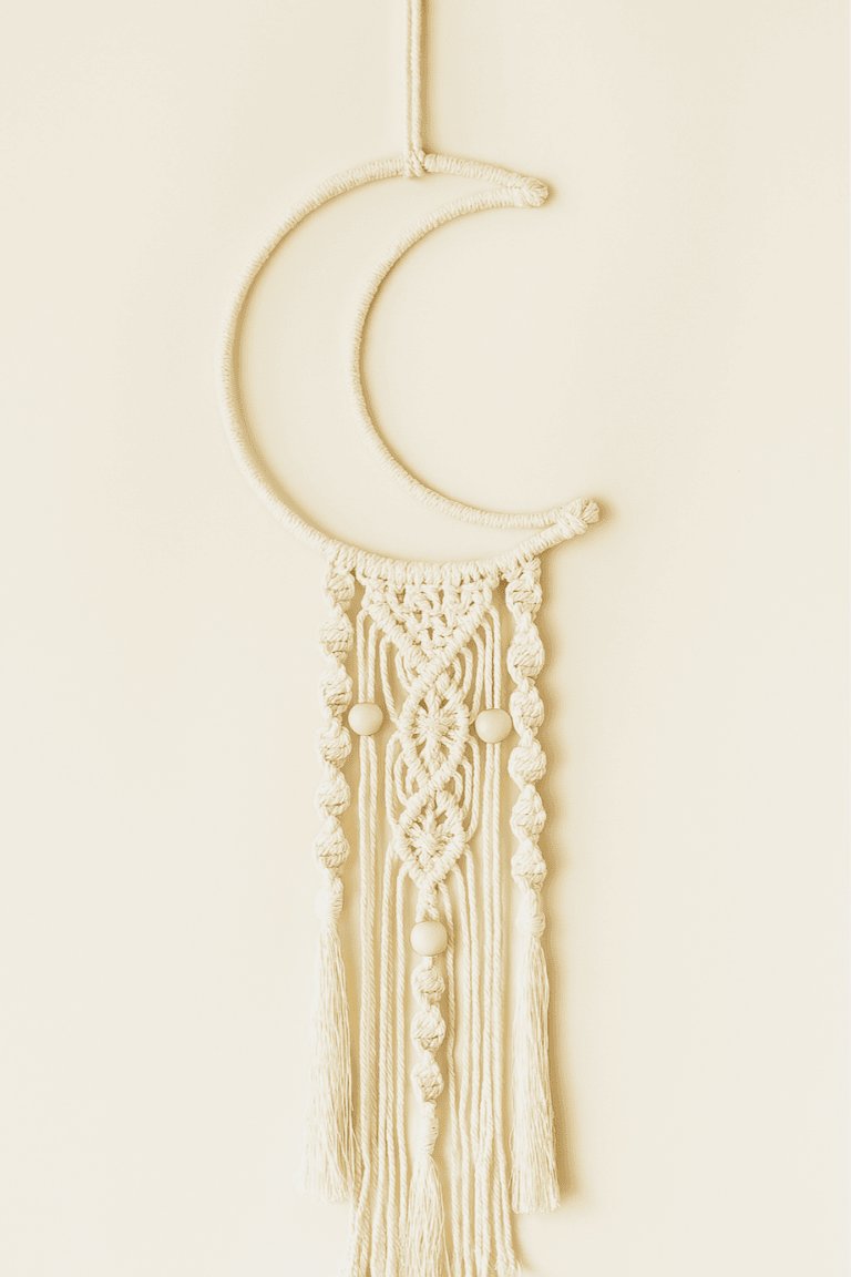 Handmade macramé crescent moon wall hanging with detailed knots and wooden bead accents in off-white cotton cord.