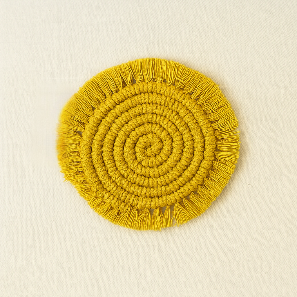 A circular macramé coaster in mustard yellow with tightly coiled knots and fringed edges, placed on a neutral beige background with the "Samra Knots" tag attached.