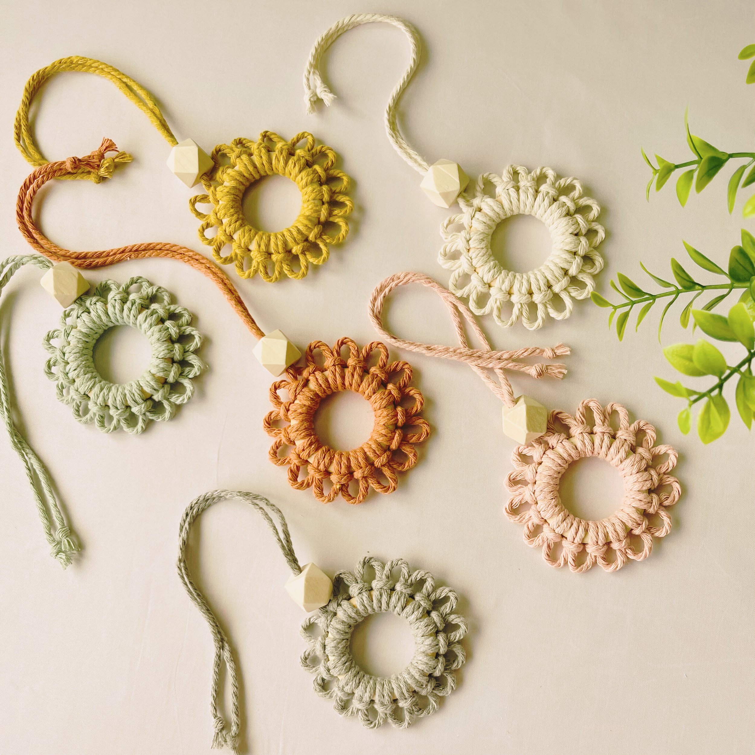 Handmade macramé car diffuser keychains in soft pastel and earthy tones, featuring wood scent beads – styled flatlay on off-white background by Samra Knots.