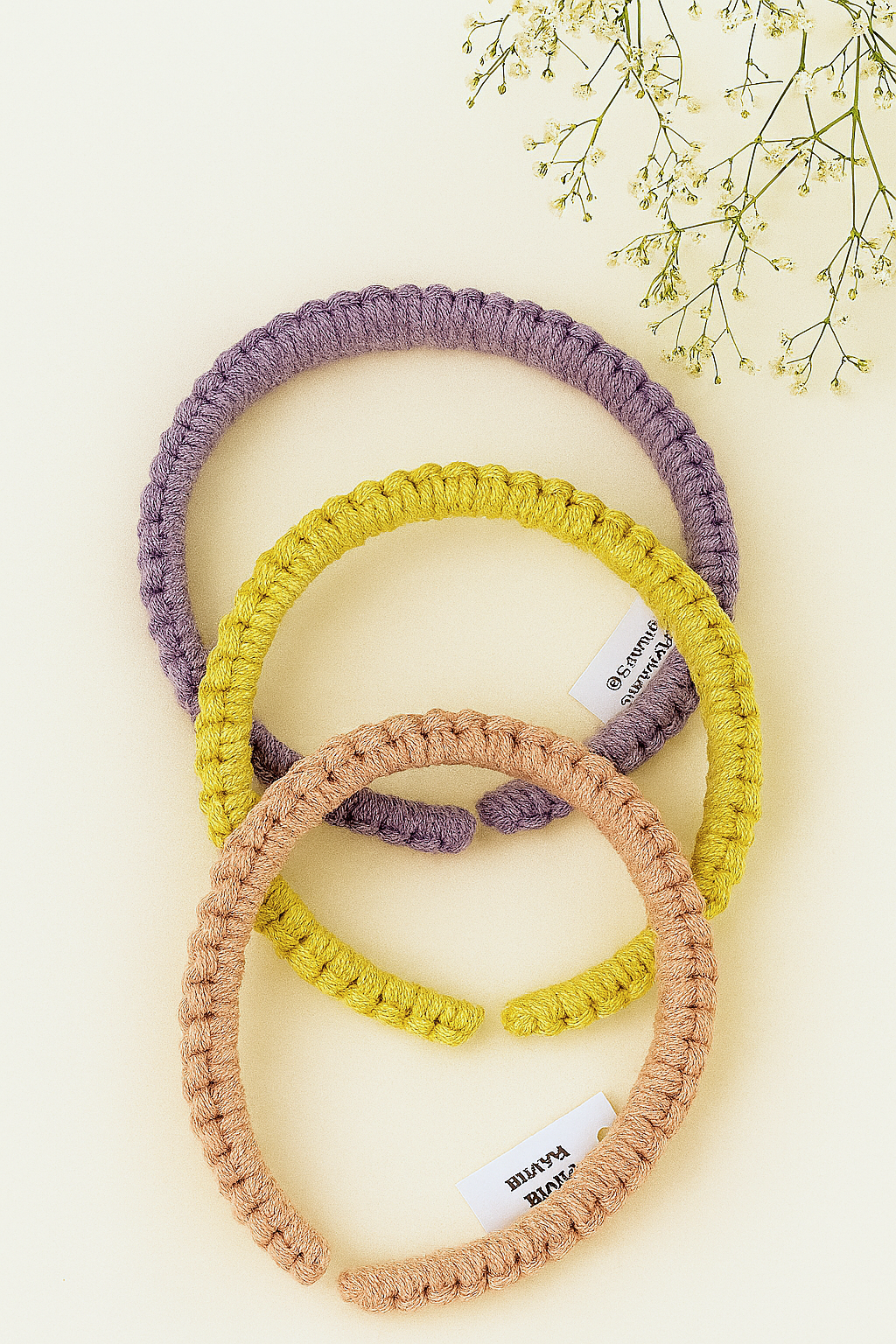 Three handmade macramé headbands in lavender, mustard yellow, and blush pink, styled on a neutral background with dried flowers – Samra Knots boho accessory.