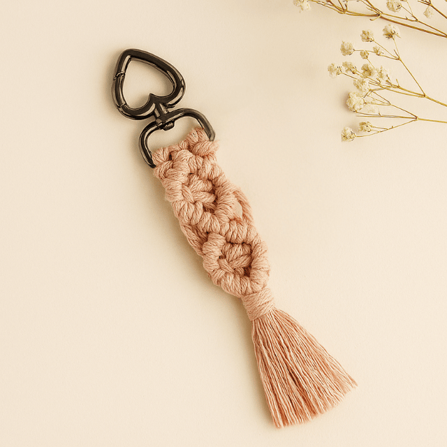 Blush pink macramé diamond keychain with black heart clasp, styled on a soft beige background with dried flowers