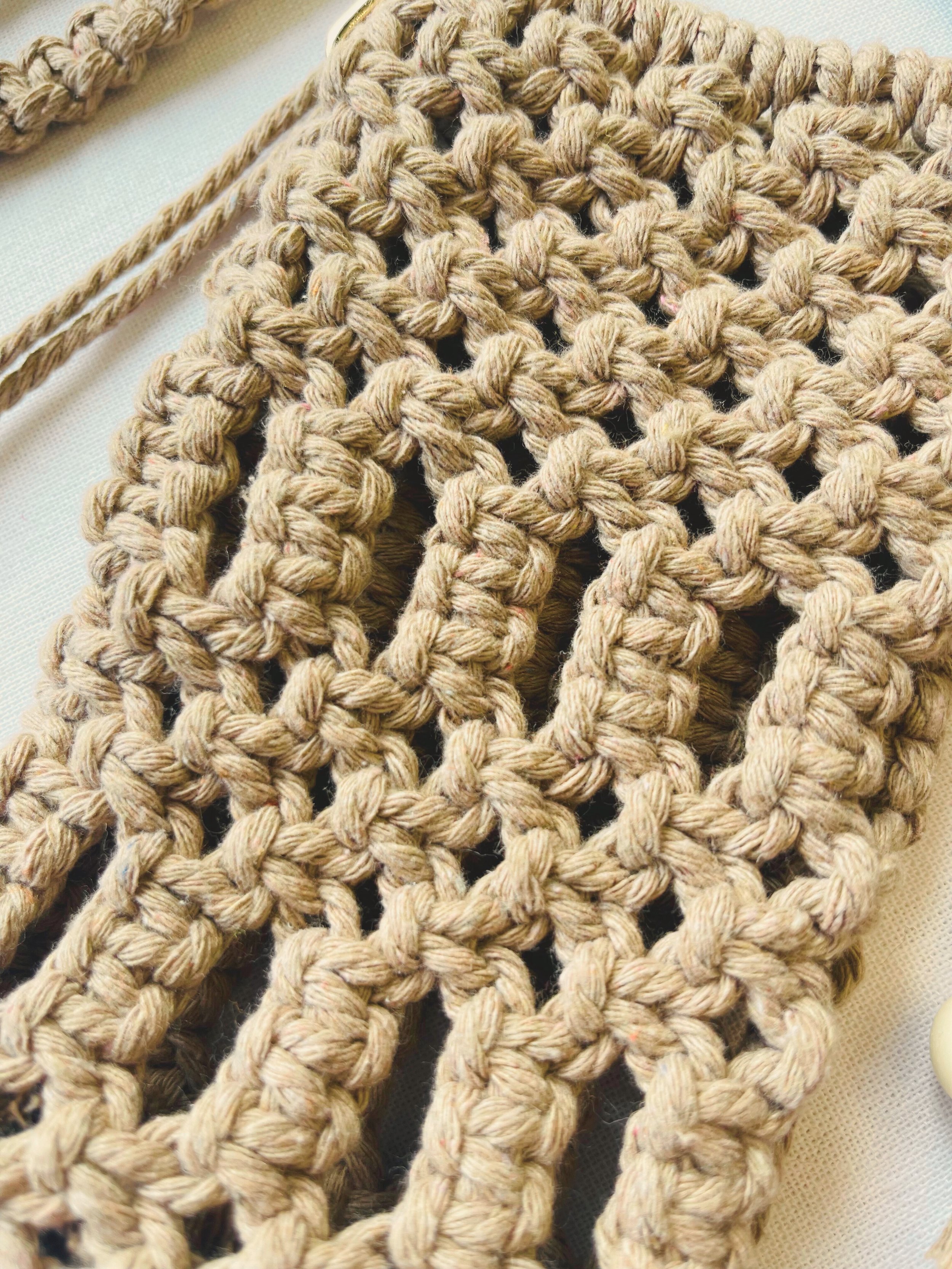 Close-up view of handmade macramé phone bag showing detailed knots in light brown cotton cord