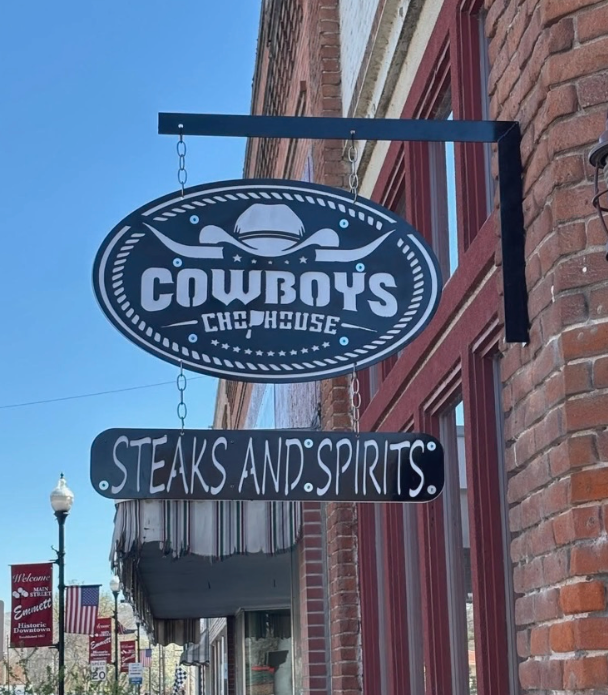 Blade Sign for Cowboy's Chop House restaurant with a cowboy hat graphic, advertising steaks and spirits, hanging on a brick building.