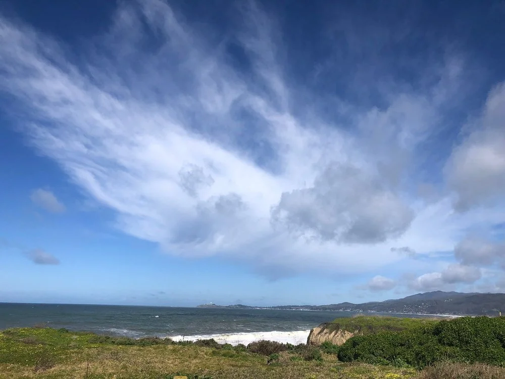 Wispy clouds sweeping over the ocean and a green coastal bluff.