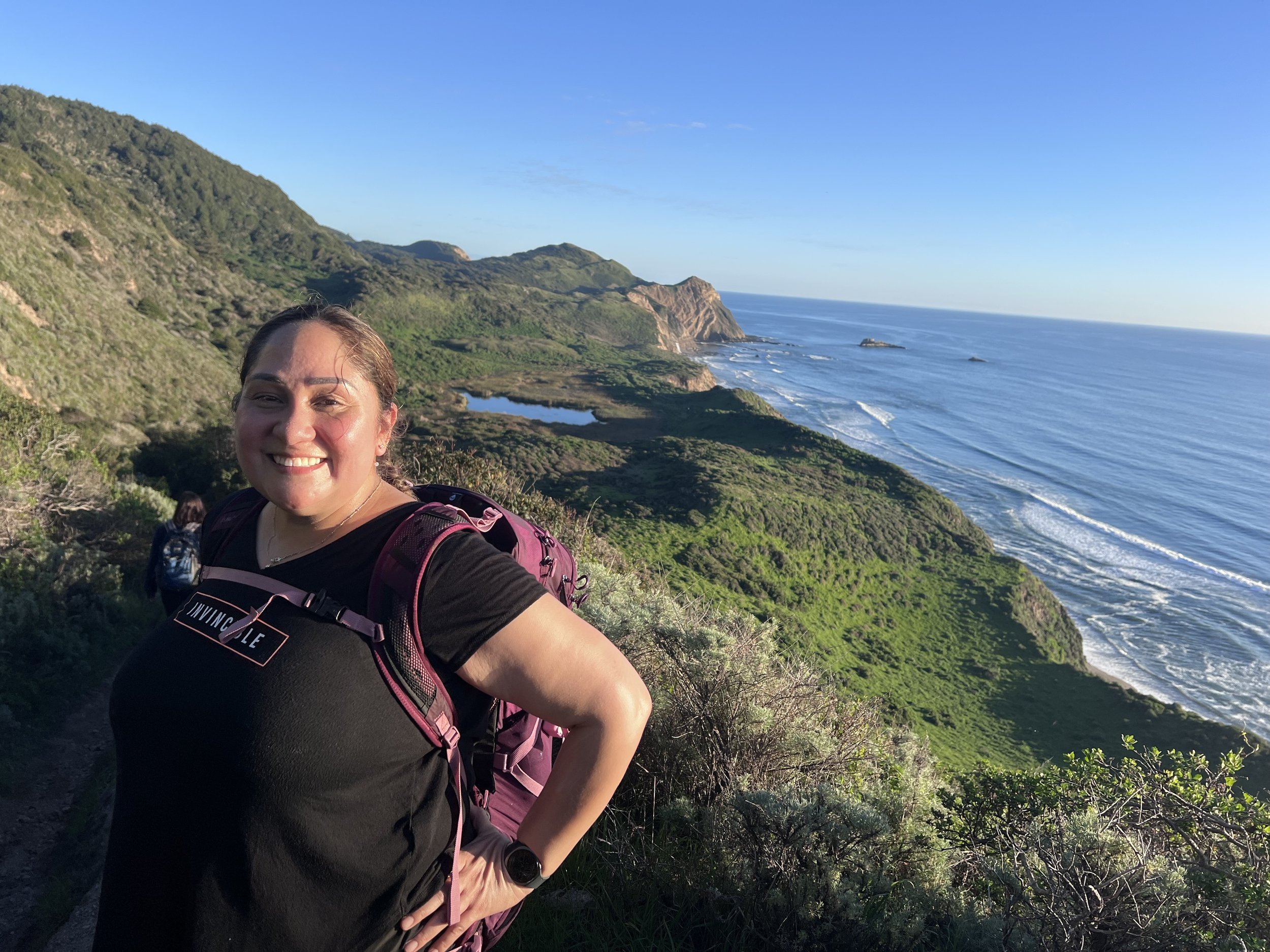 A woman smiling on a coastal bluff high above the ocean at Point Reyes.