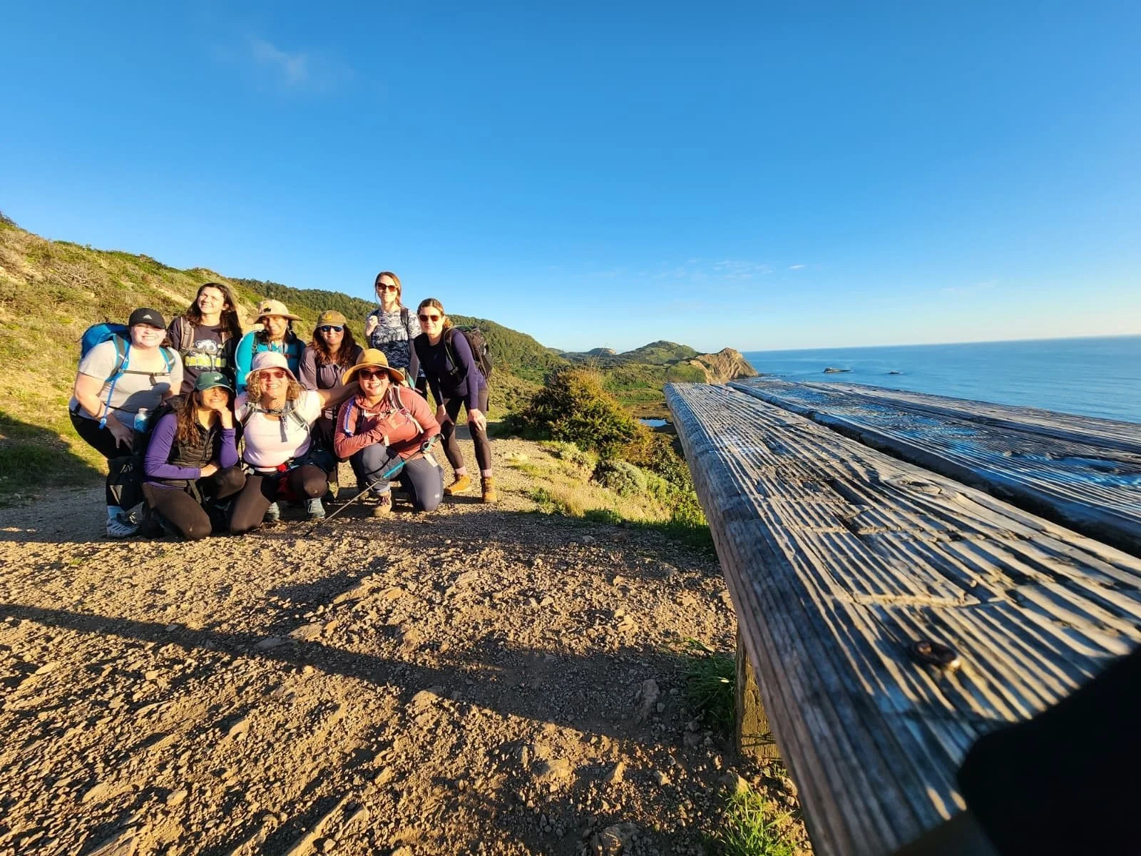 A group of women posing on a coastal trail above the ocean at Point Reyes.
