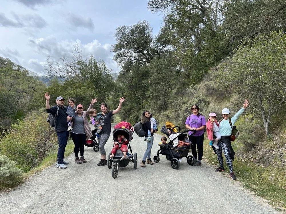 Families with strollers waving on a wide dirt trail at Little Yosemite in the East Bay.
