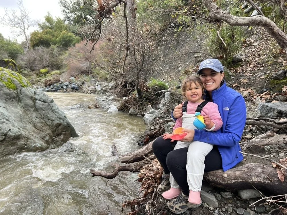 A parent and toddler sitting on a log beside a rushing creek at Little Yosemite in the East Bay.