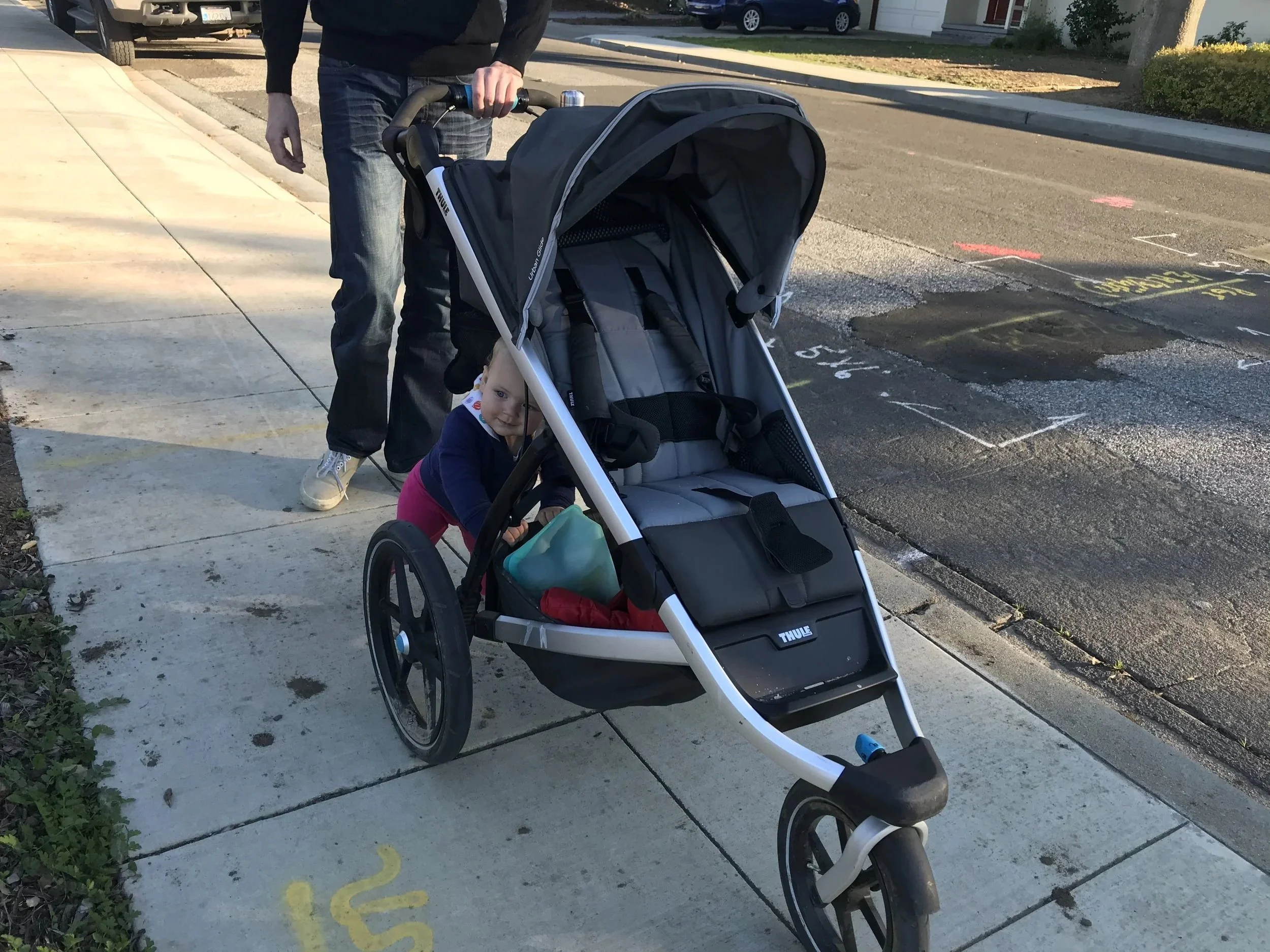 A Thule jogging stroller with a child inside, pushed along a sidewalk.