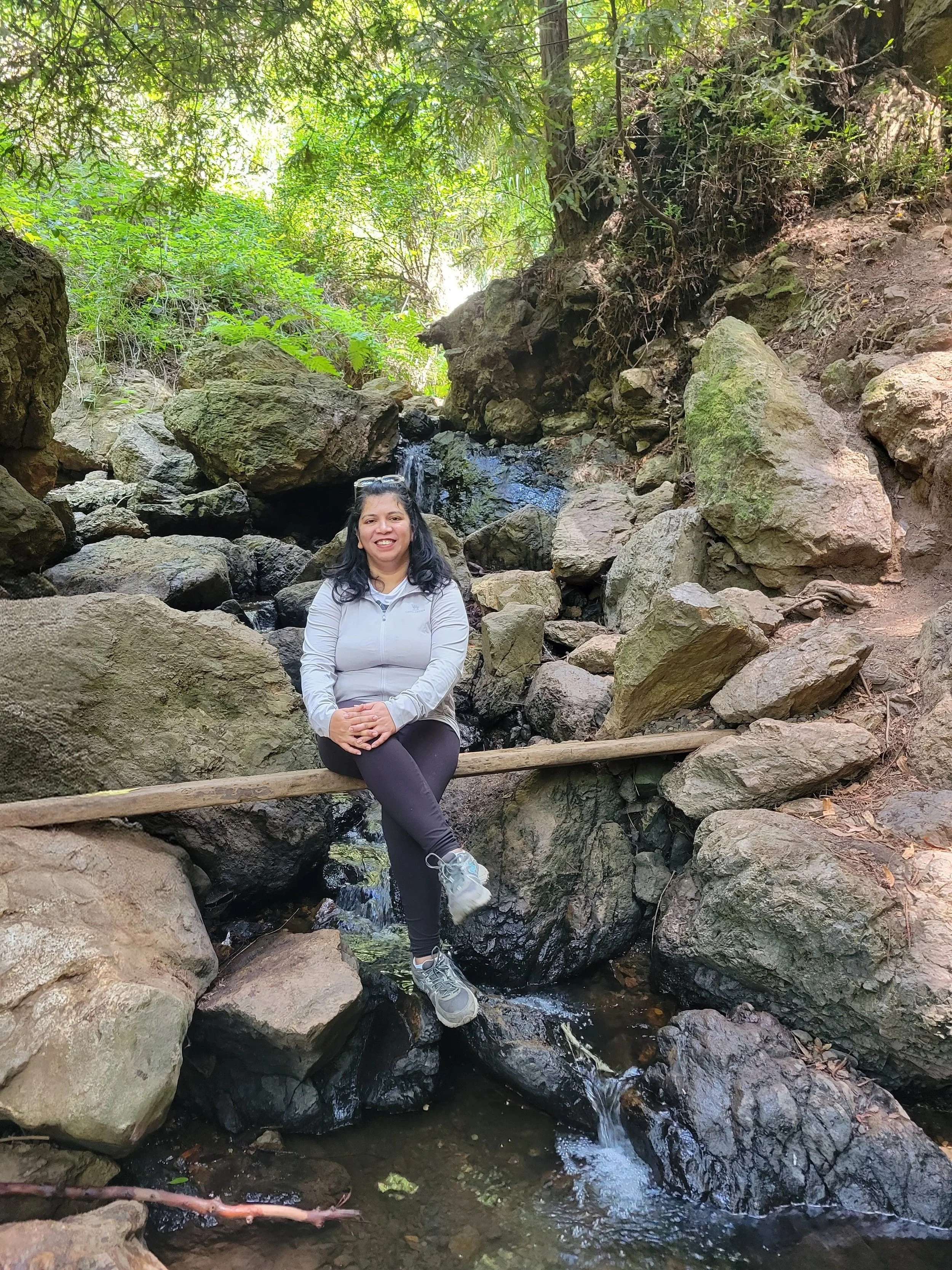 Pranali Lad, Family Adventure Squad hike planner, smiling in front of a small waterfall on a hike
