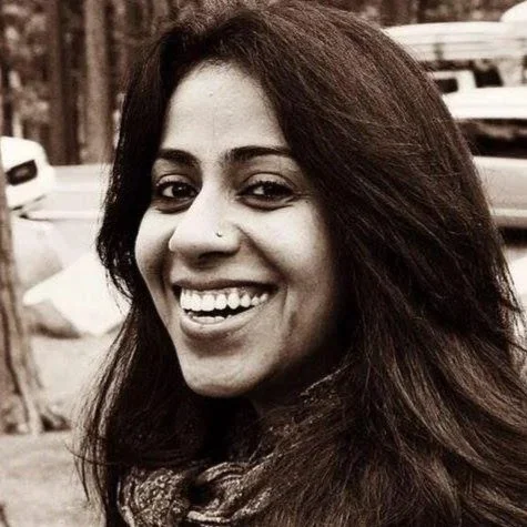 Sepia portrait of Sneha Mahecha, Family Adventure Squad writer, smiling among tall pine trees