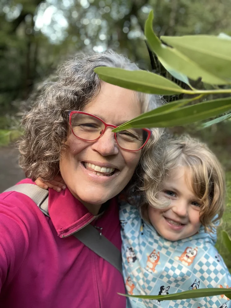Family Adventure Squad founder Miranda and her young daughter smiling together under bay laurel leaves on a forest hike