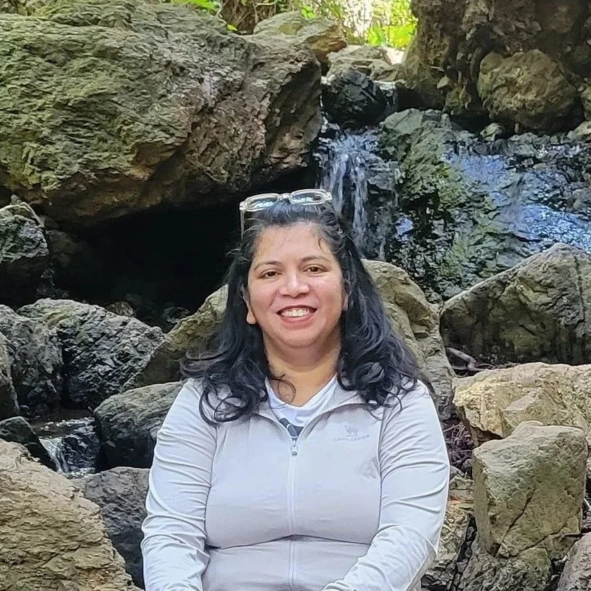 Pranali Lad, Family Adventure Squad hike planner, smiling in front of a small waterfall on a hike
