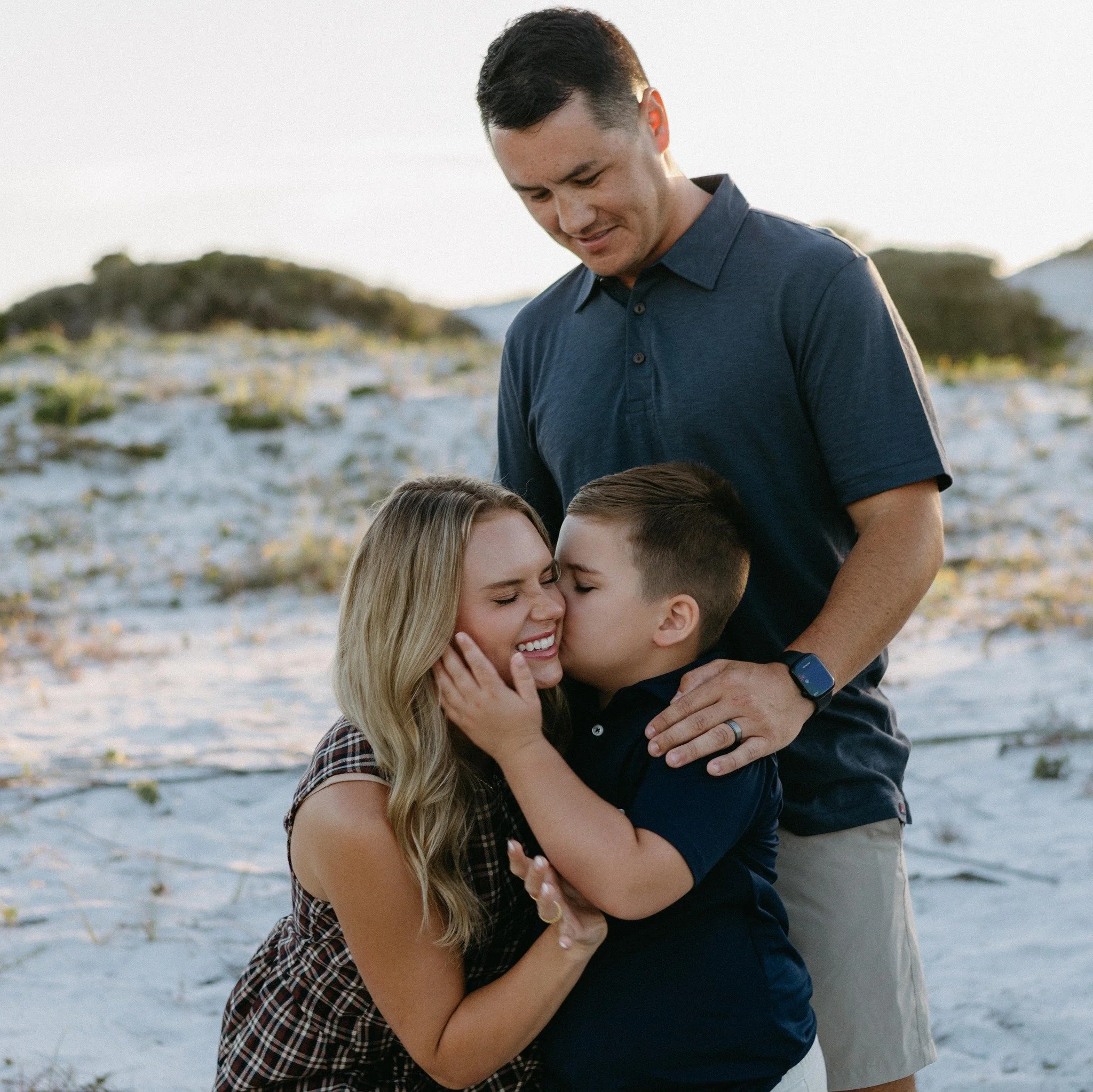 A family of four on a beach, smiling and hugging each other.