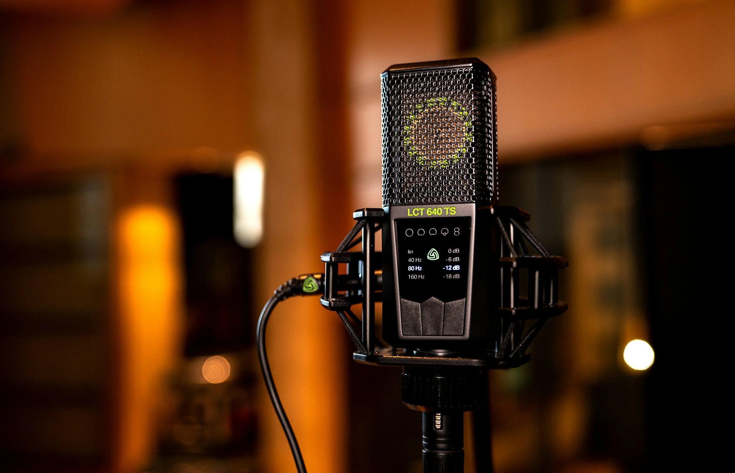 Close-up of a studio microphone labeled LCT 640 TS with a suspension mount and cable in a dimly lit recording studio.