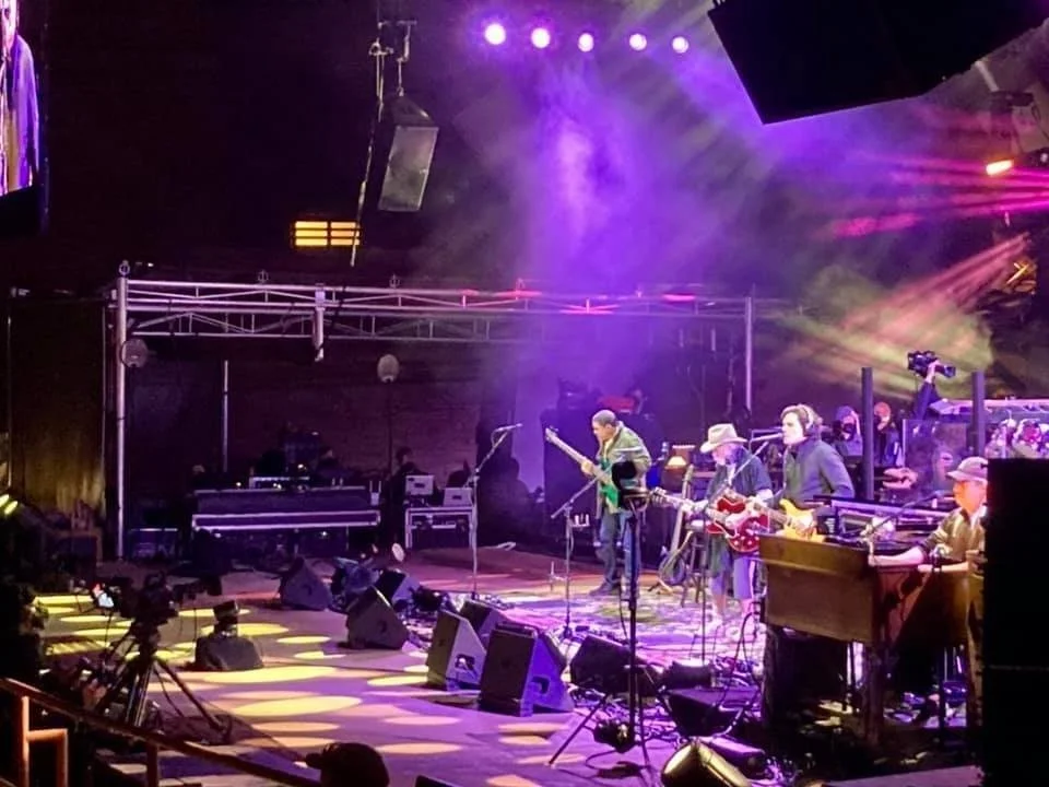 Musical band performing on an illuminated stage with colorful lights and equipment.