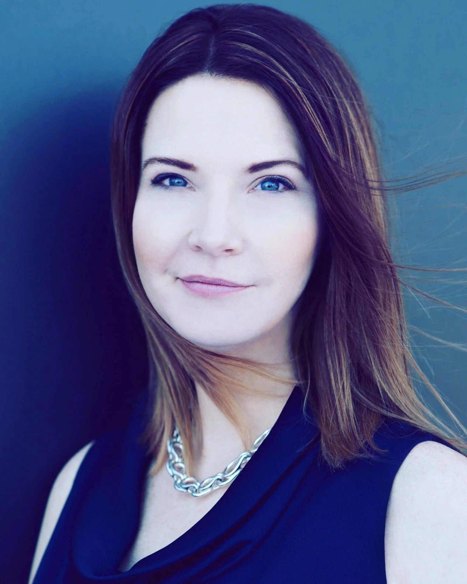Woman with brown hair and blue eyes wearing a black top and silver necklace