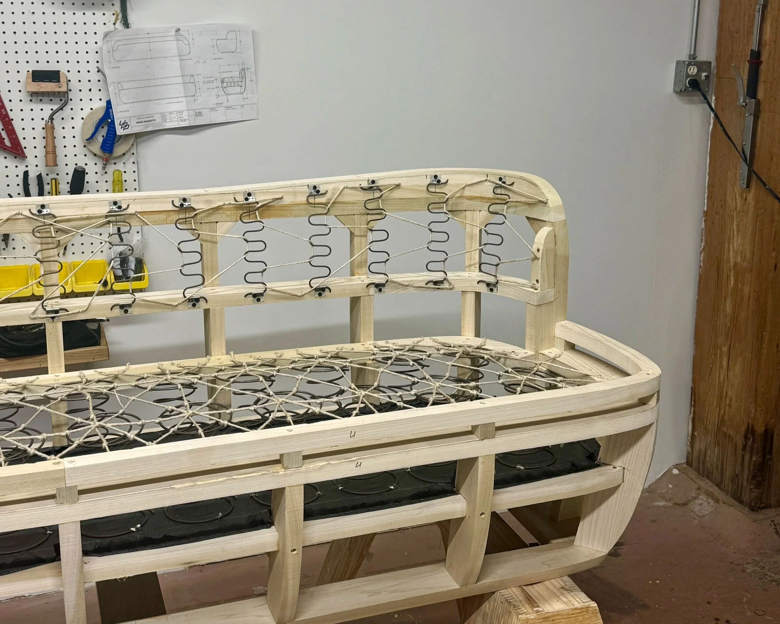 Wood upholstery frame resting on a concrete floor against a white wall.