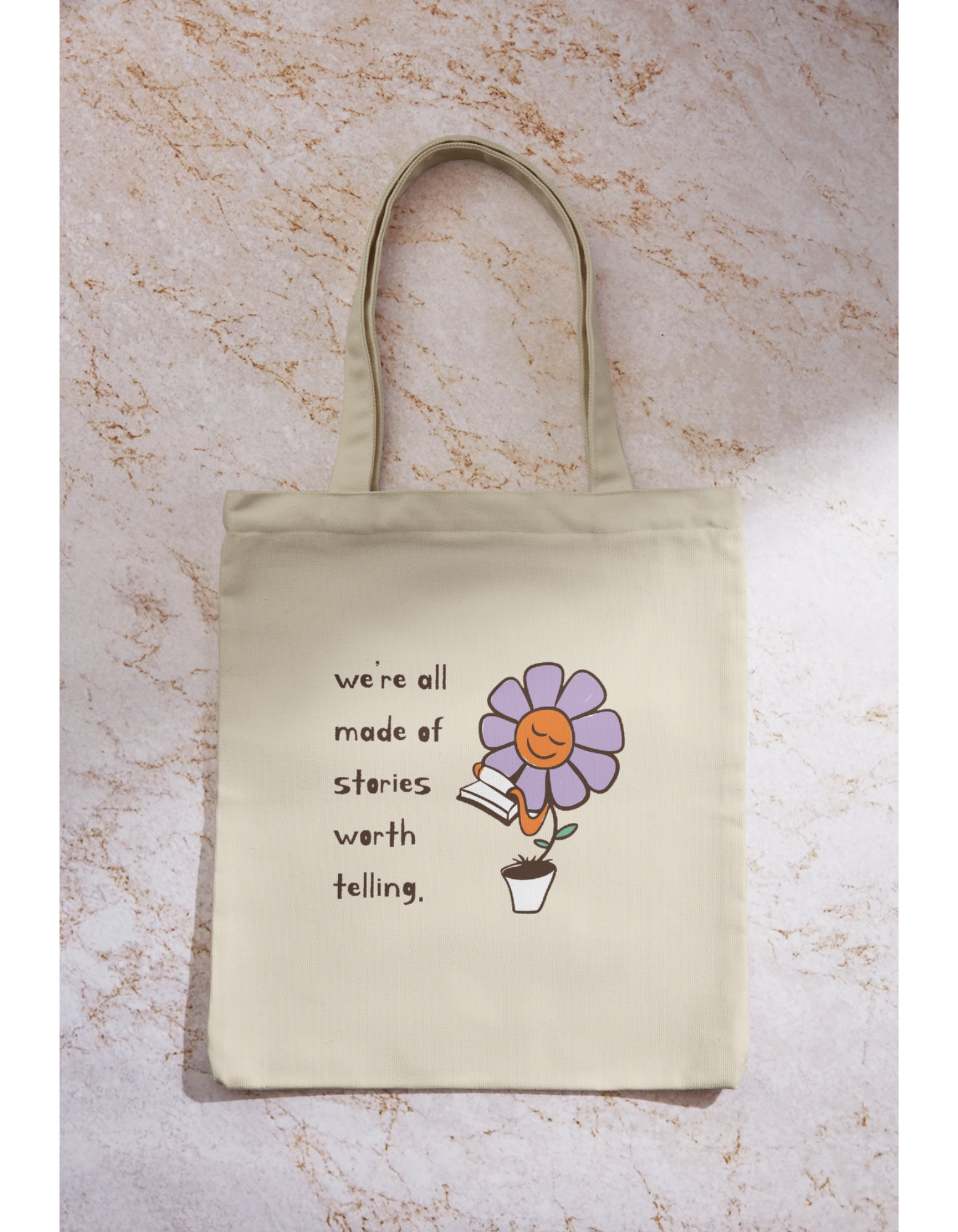 Beige tote bag with a cartoon flower holding a book and smiling. Text reads, 'we're all made of stories worth telling.'