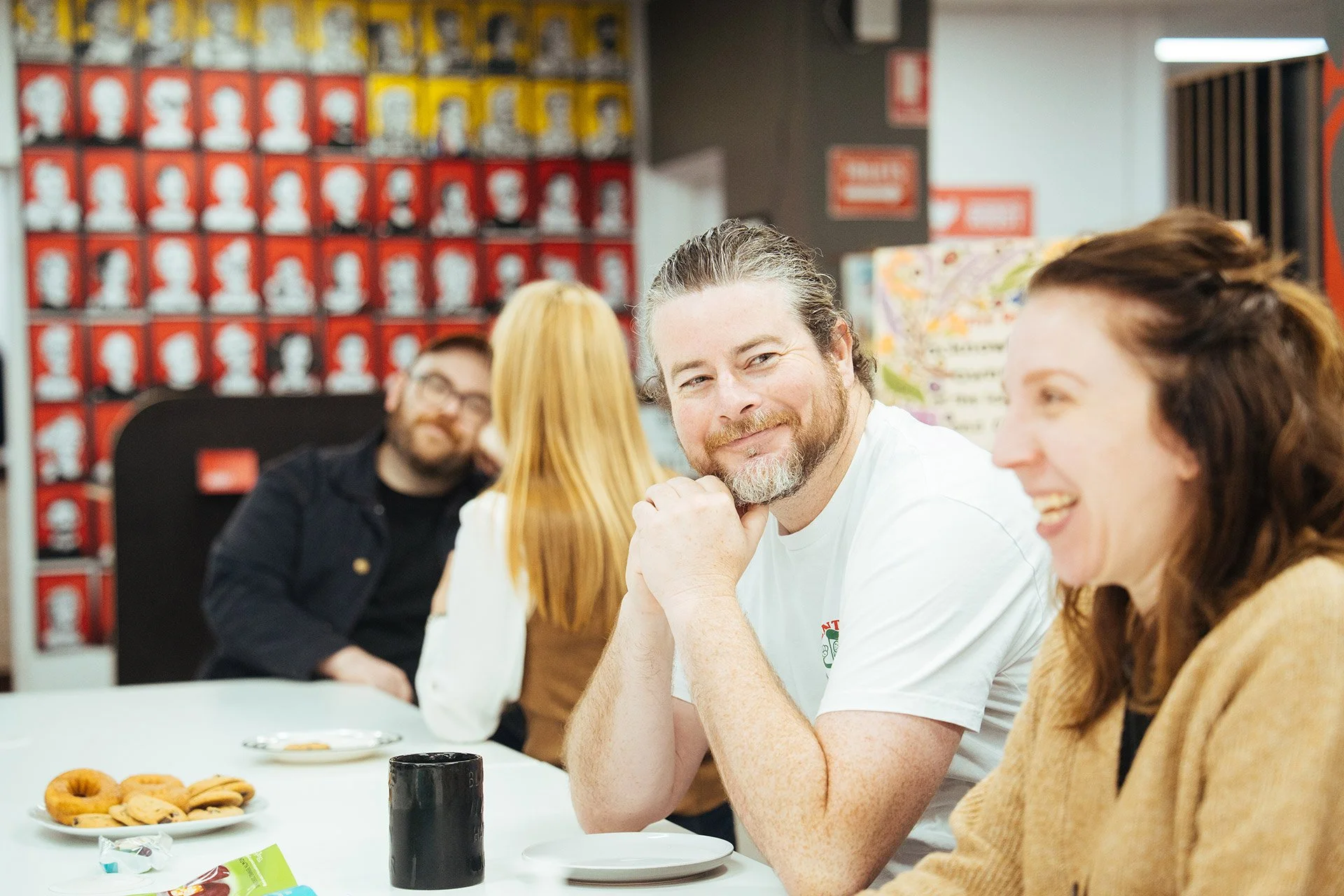 Group of four people sitting at a table, smiling and talking, in a room with artwork on the wall.