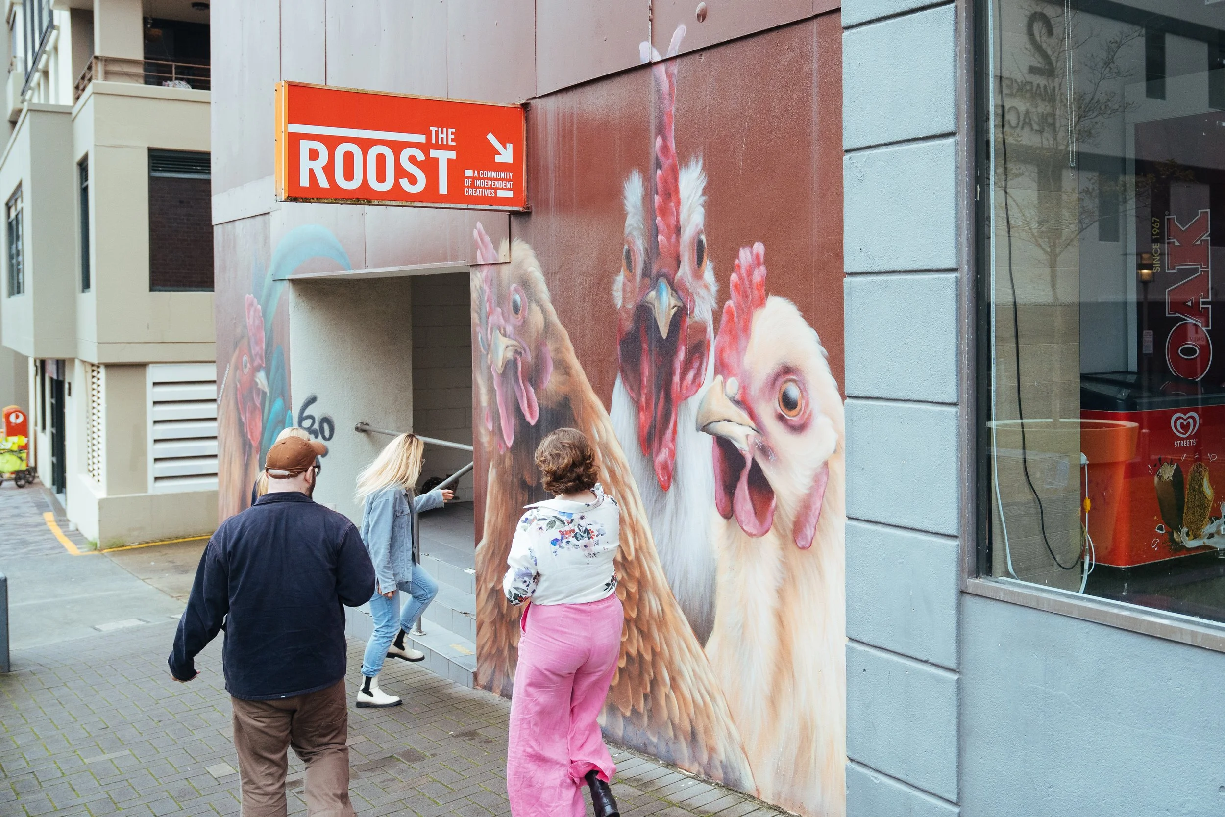 Street mural of chickens on the wall of a building with three people walking past
