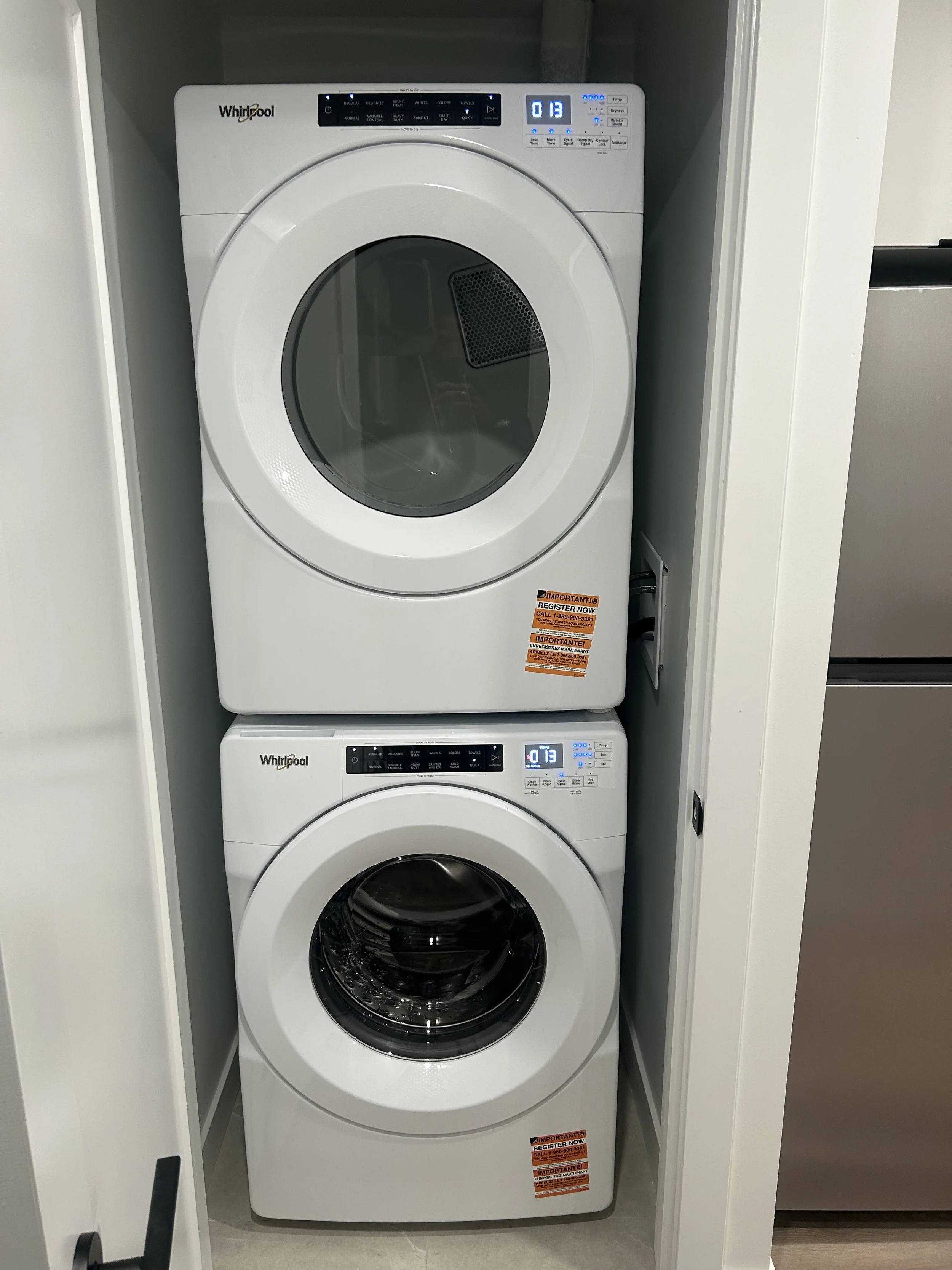 Stacked white Whirlpool washer and dryer in a narrow closet with a gray wall.