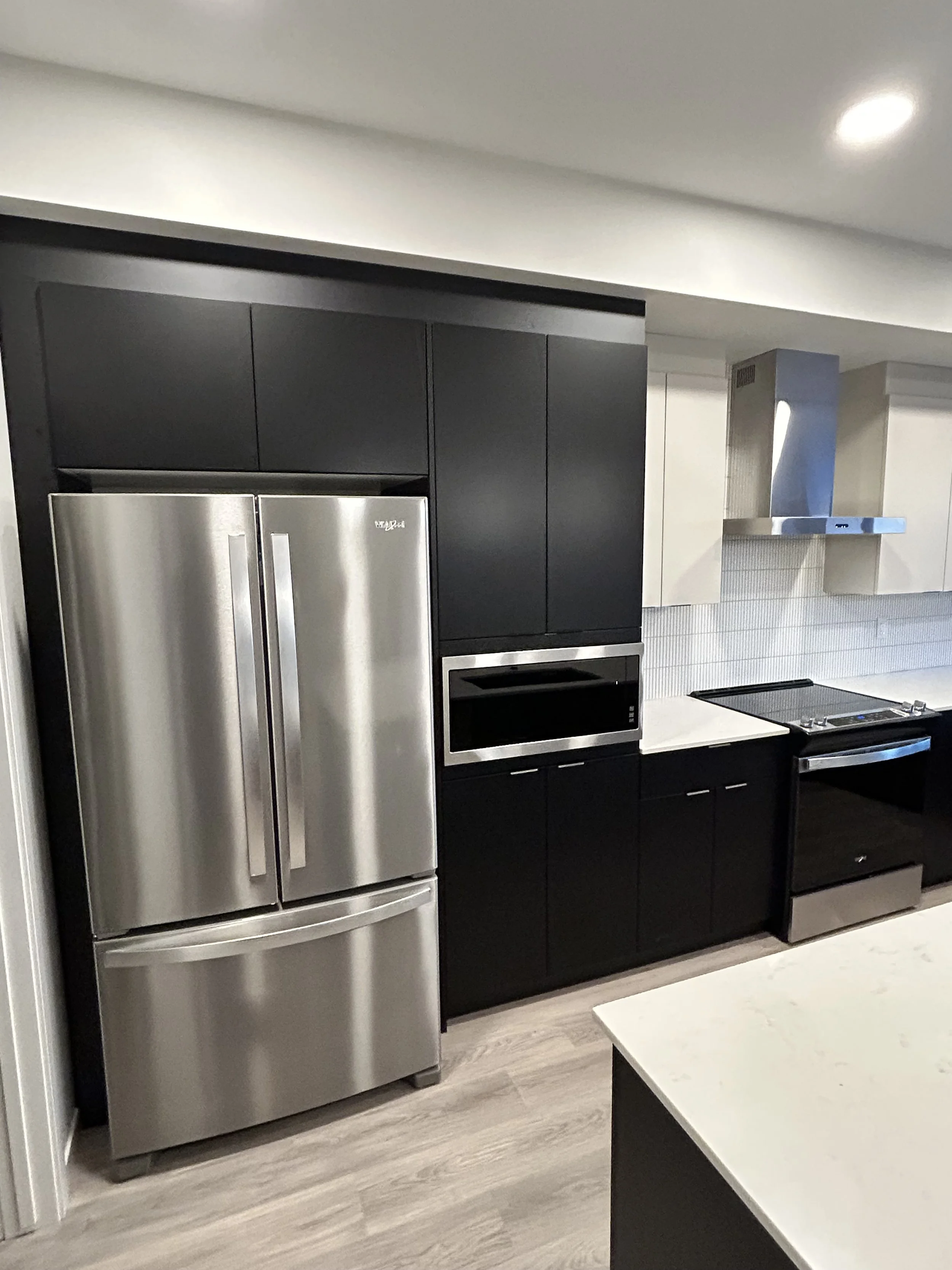 Modern kitchen with stainless steel refrigerator, black cabinets, white countertops, stainless steel range hood, and a black stove.