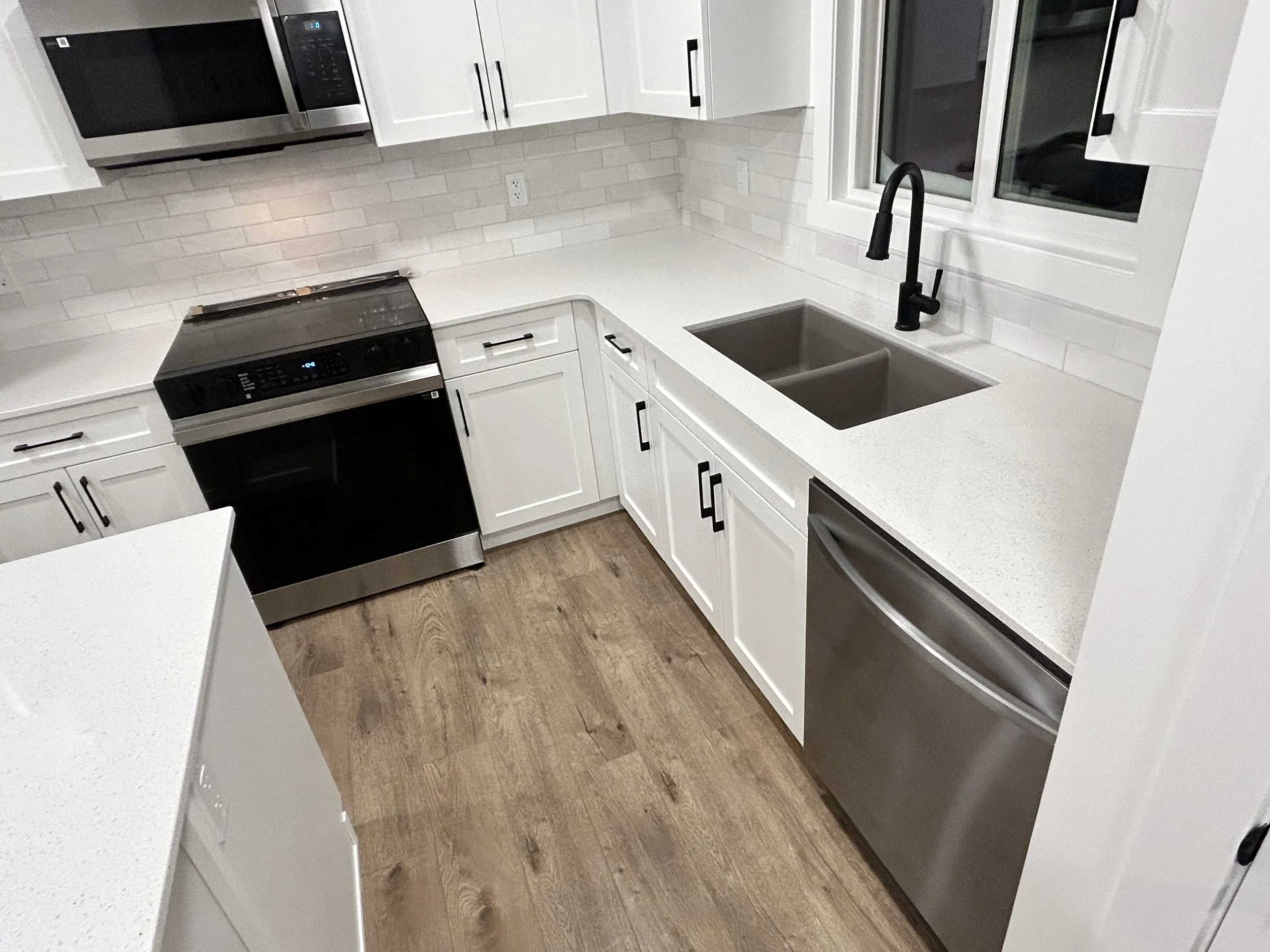 Modern kitchen with white cabinets, black hardware, stainless steel appliances, a black faucet, a double sink, and wood flooring.