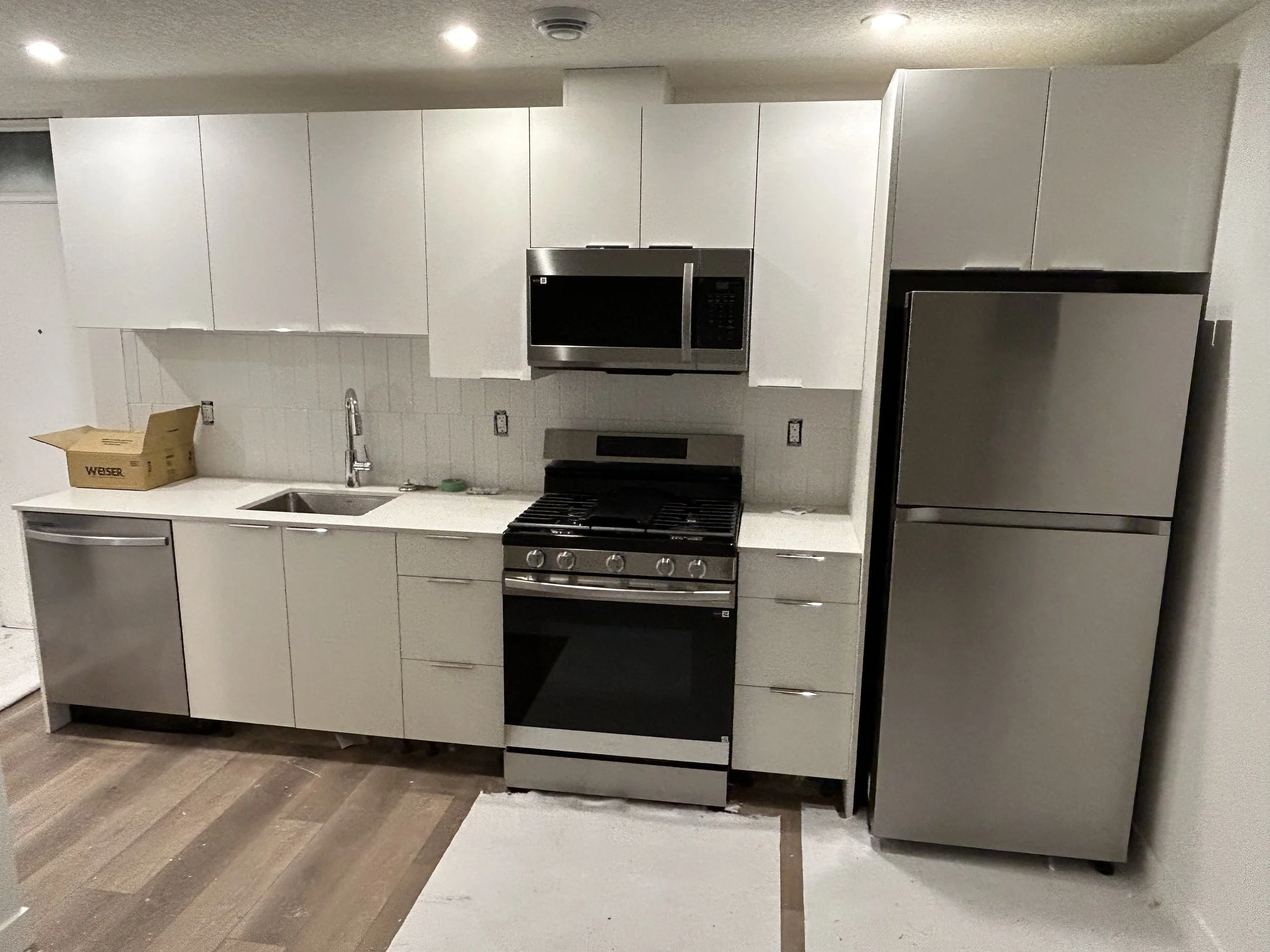 Modern kitchen with white cabinets, stainless steel appliances, and wooden flooring.