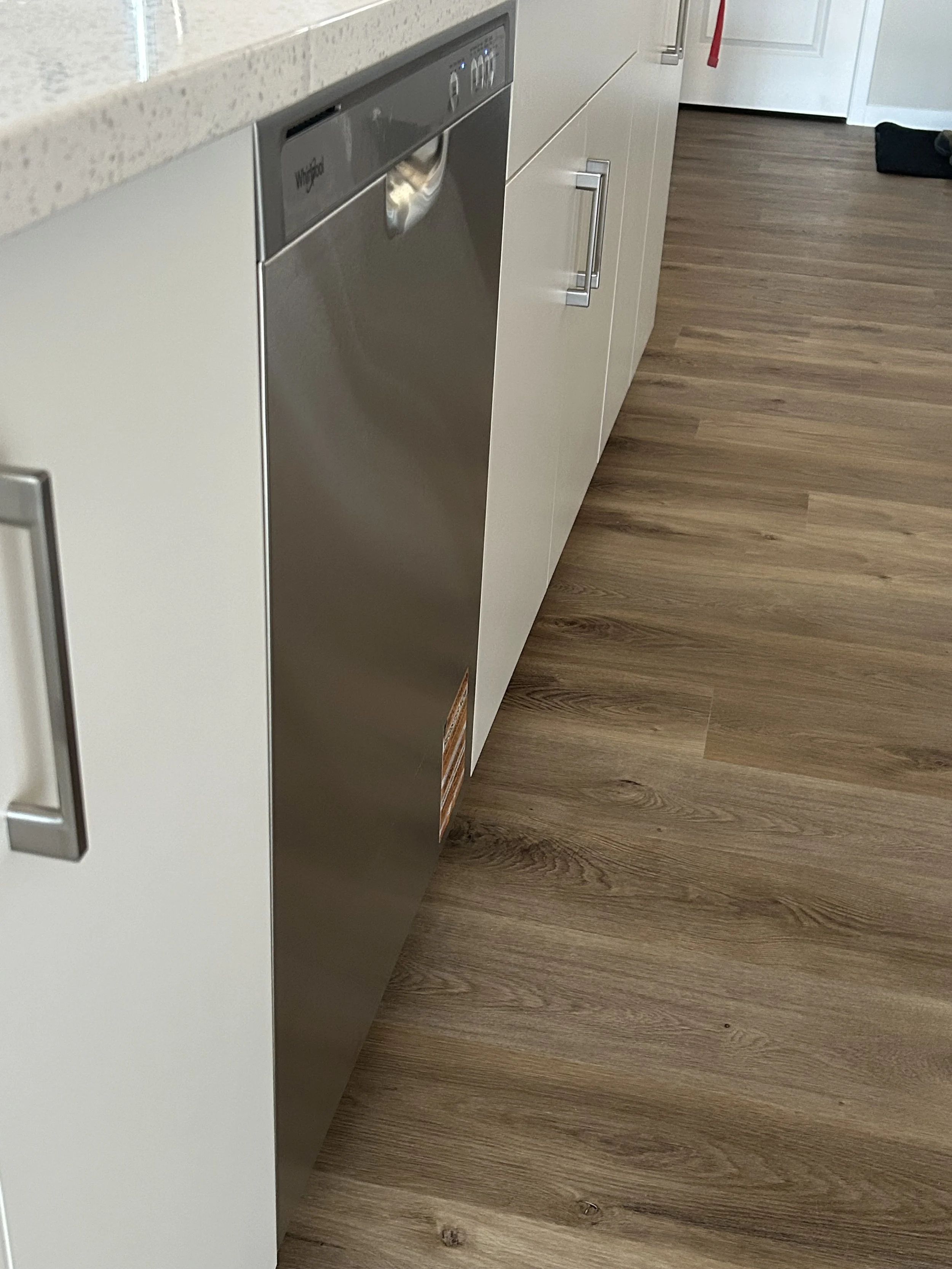 A kitchen with a beige countertop, white cabinets, a stainless steel dishwasher, and hardwood flooring.