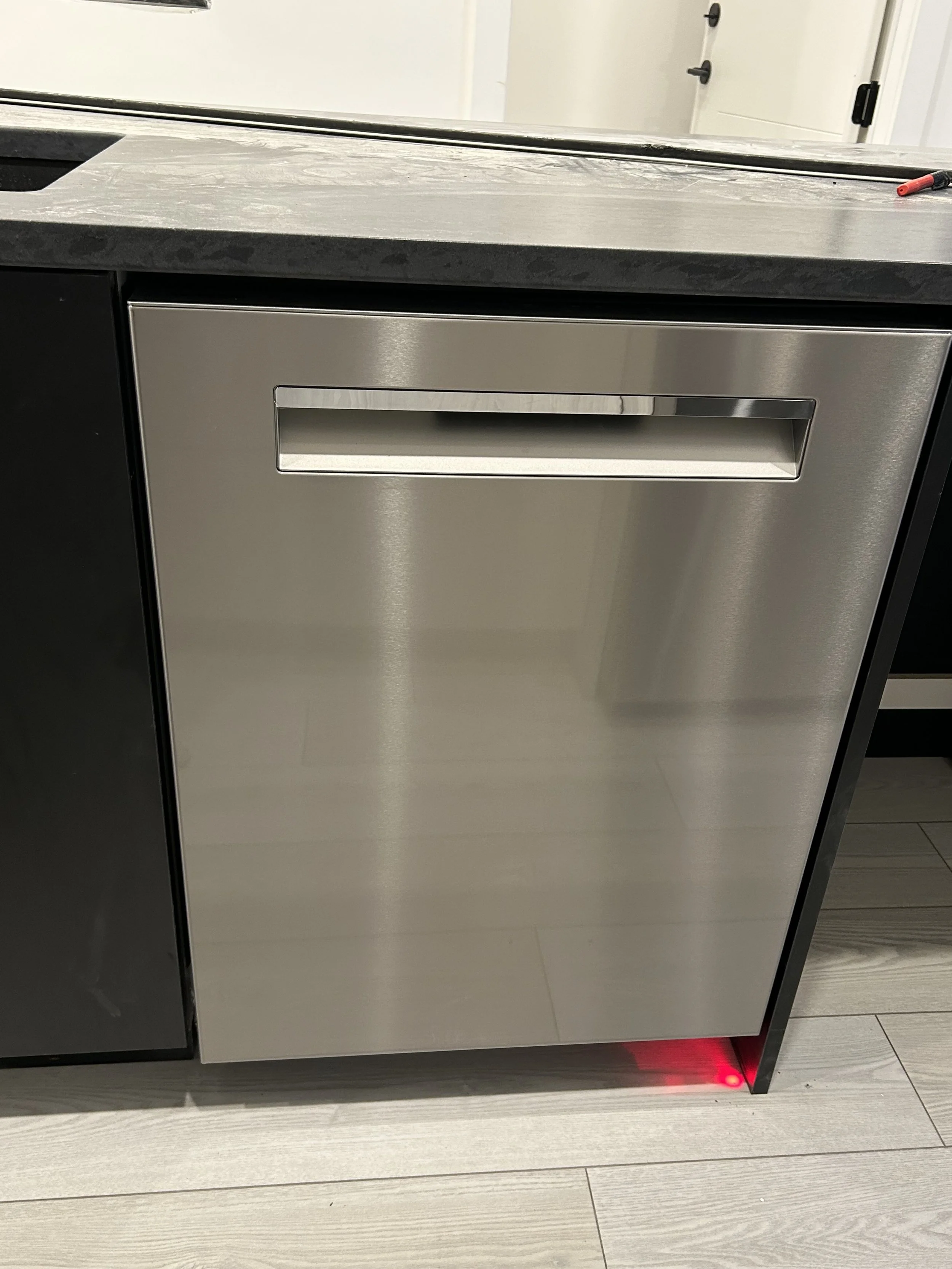 Stainless steel dishwasher in a modern kitchen with grey countertops and wooden flooring.
