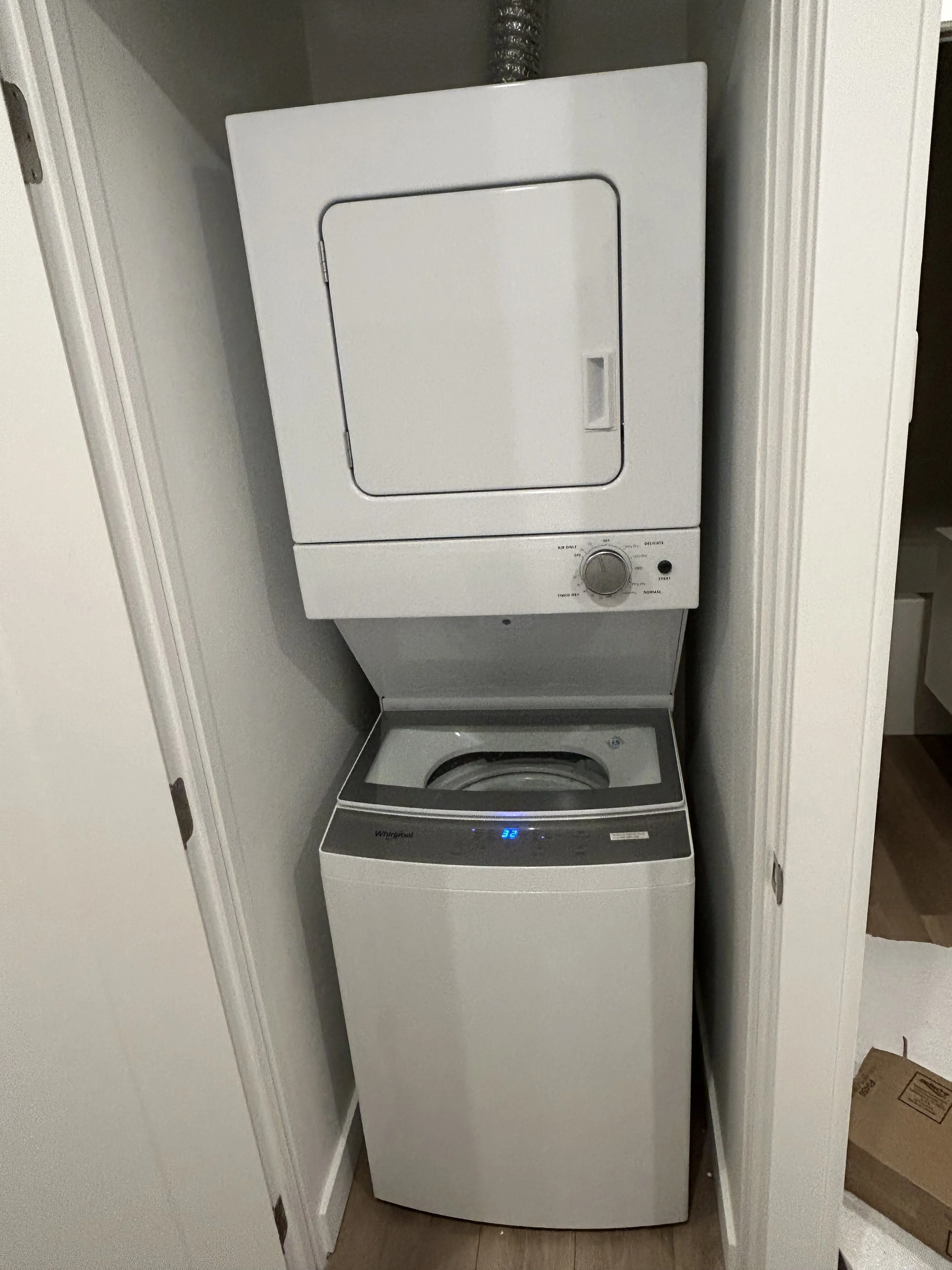 A stacked washer and dryer in a laundry closet, with the washer on the bottom and the dryer on top, both white with control panels.
