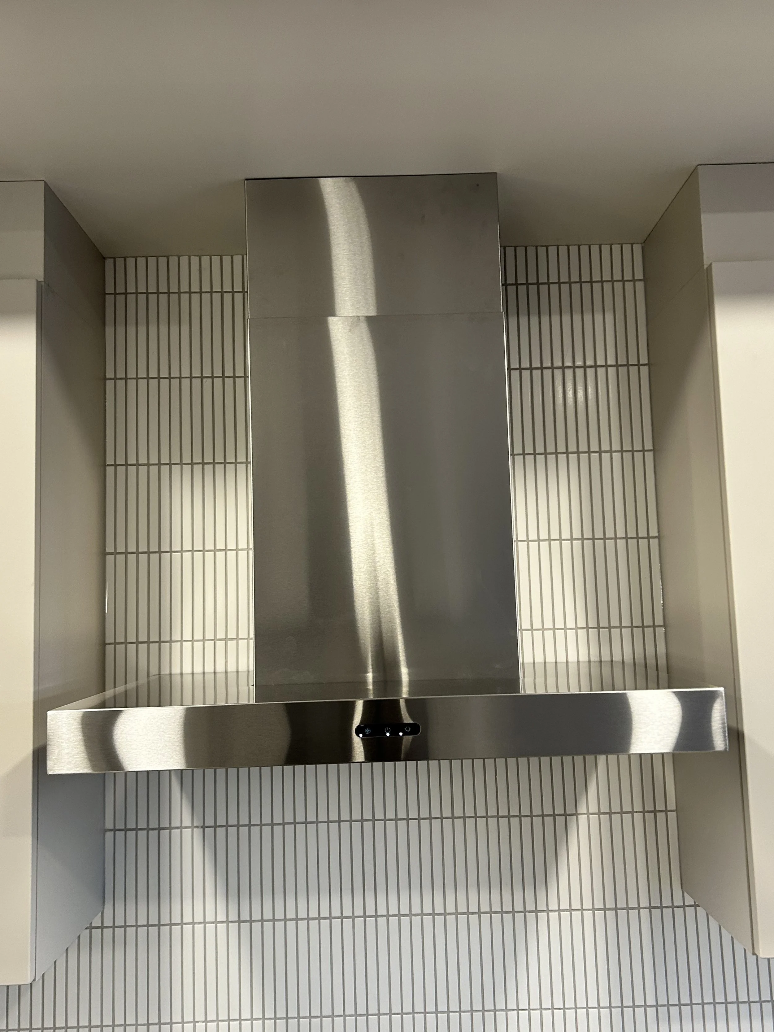 Stainless steel elevator panel in a tiled wall with control buttons.