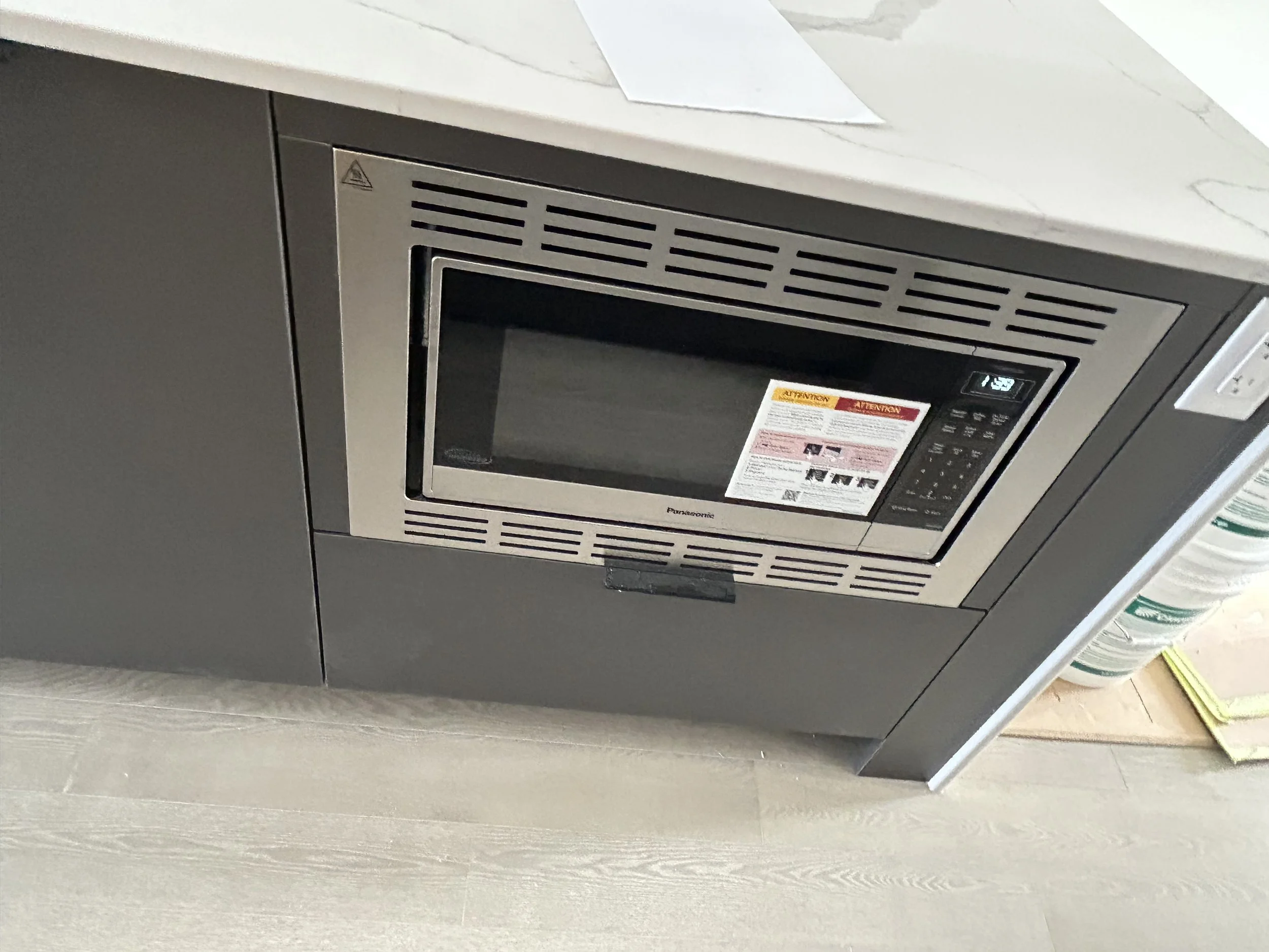 Stainless steel microwave oven installed in a modern kitchen with a white marble countertop and a gray cabinet below.
