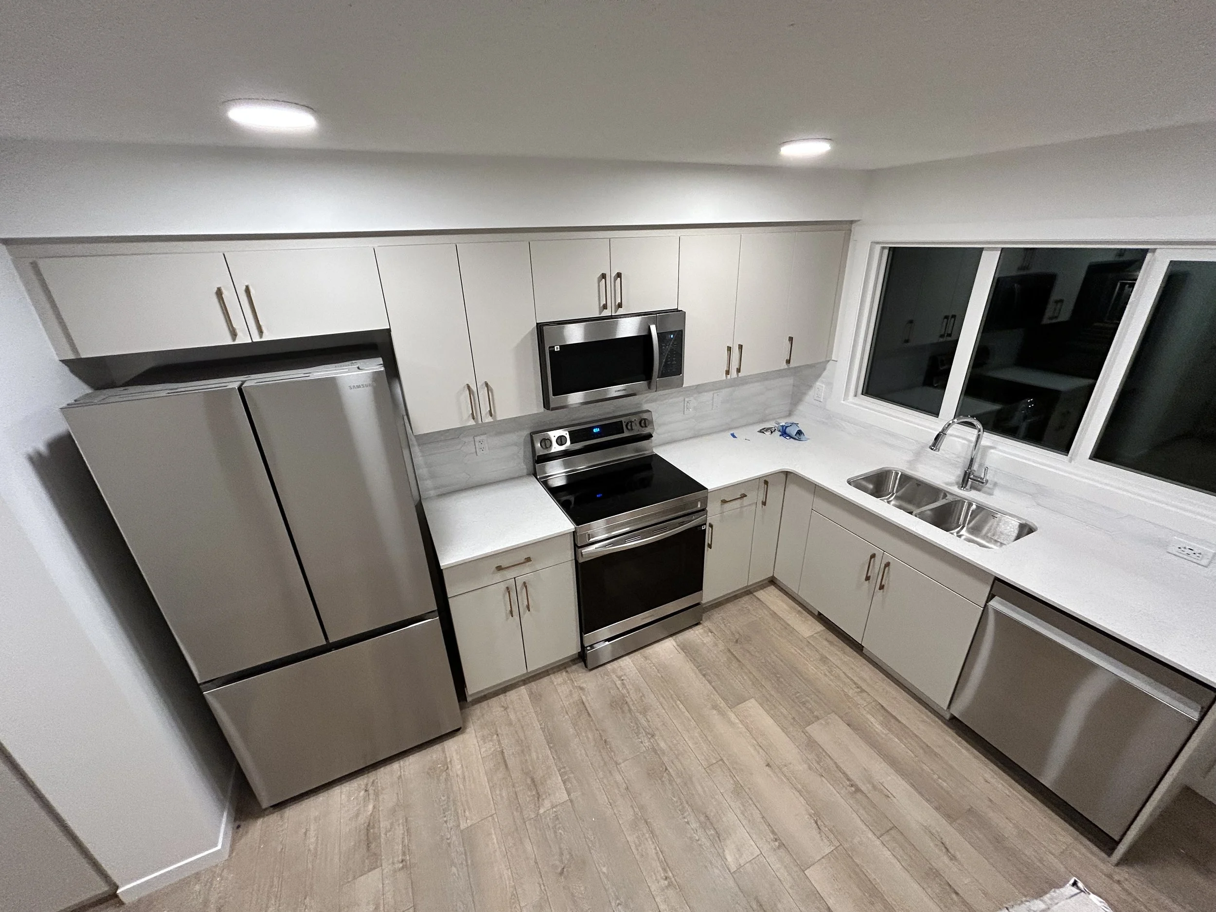 A modern kitchen with white cabinets, stainless steel appliances, a double sink, and a large window over the countertop.