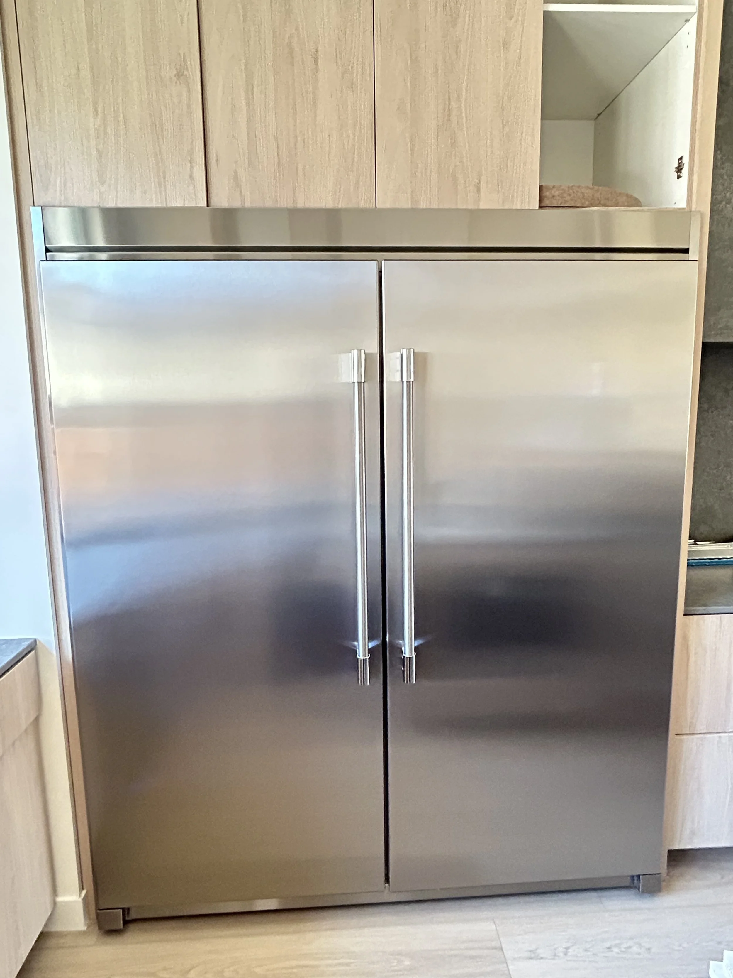 Stainless steel double-door refrigerator in a kitchen with wooden cabinets.