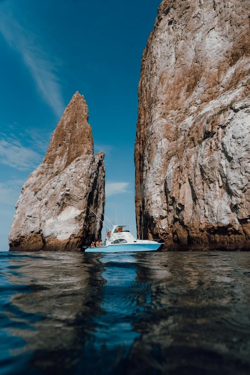 Boat navigating between tall rocky cliffs in the ocean under a blue sky.