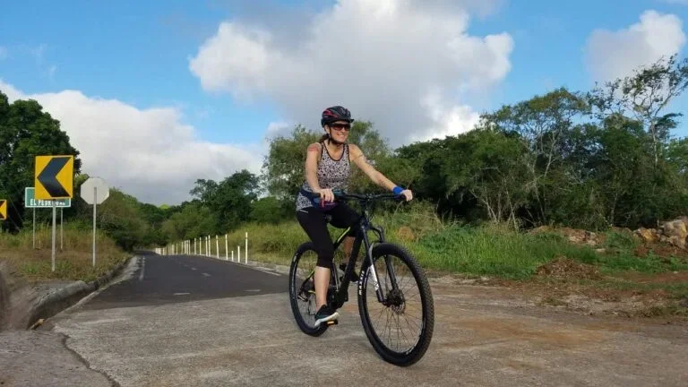 A woman biking on a dirt trail in the highlands of San Cristóbal Island, Galápagos, surrounded by lush farmland and scenic landscapes